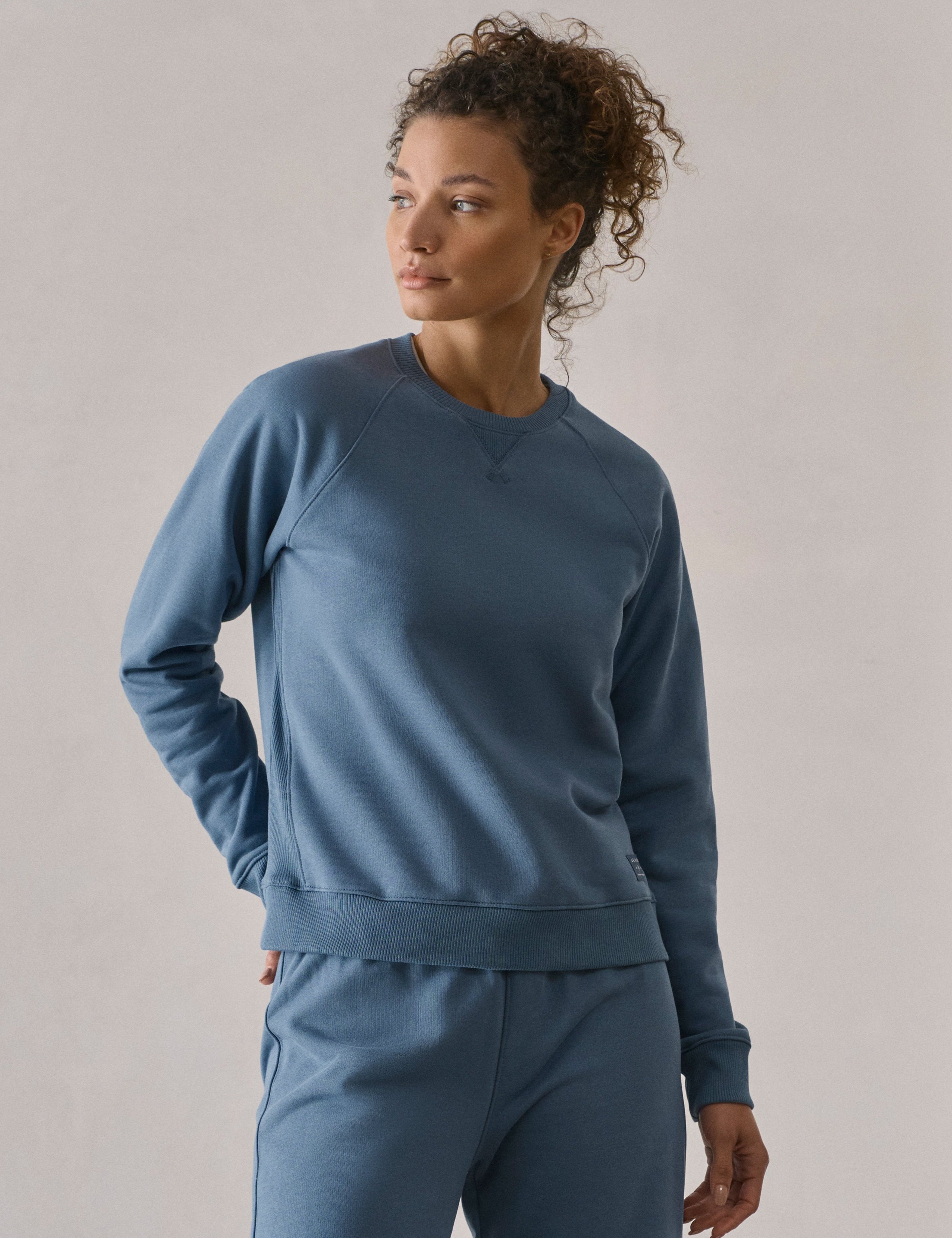 Front 3/4 upper-body view of woman wearing W Osa Raglan Sweatshirt in Coastal Blue from AETHER Apparel.