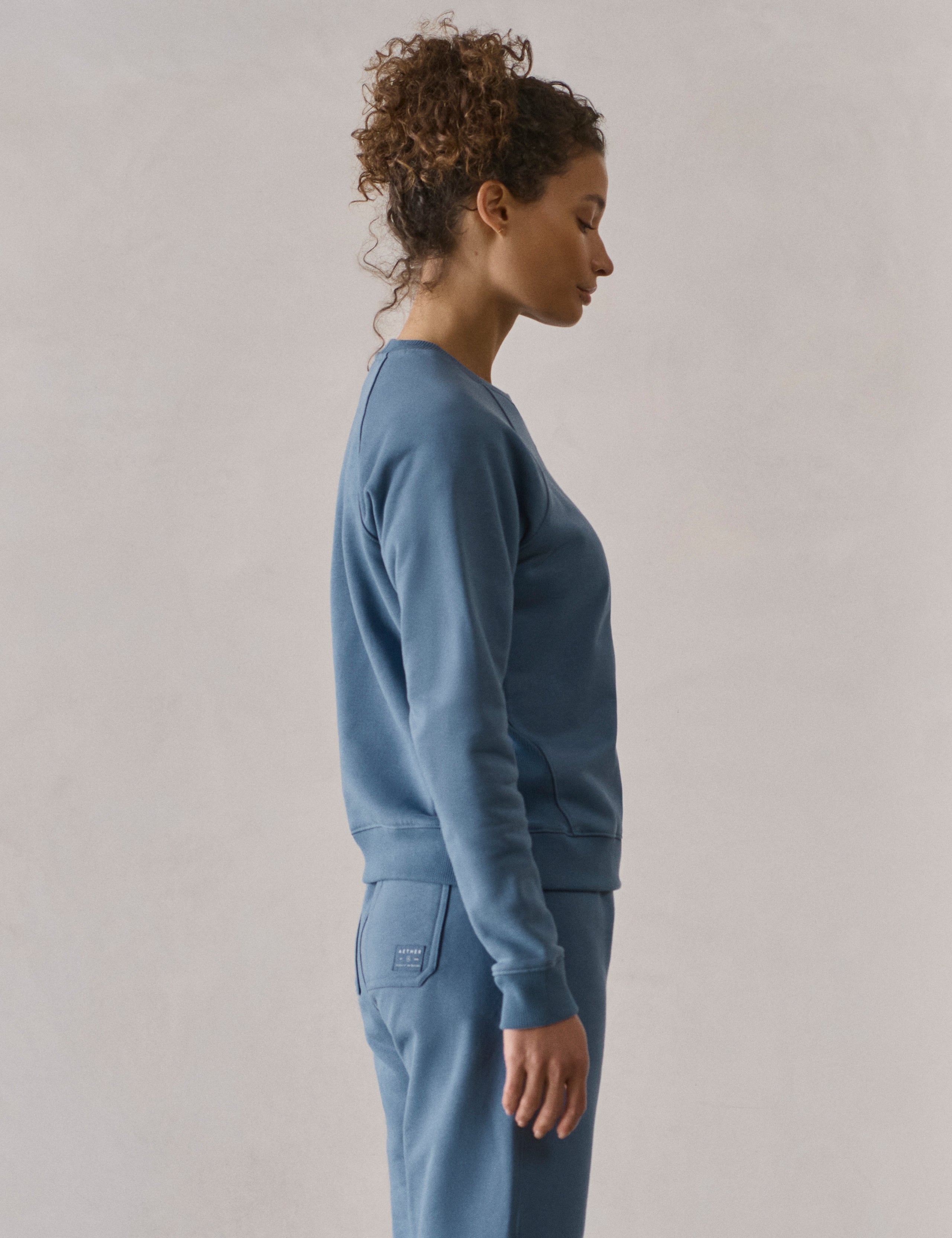 Right side profile upper-body view of woman wearing W Osa Raglan Sweatshirt in Coastal Blue from AETHER Apparel.
