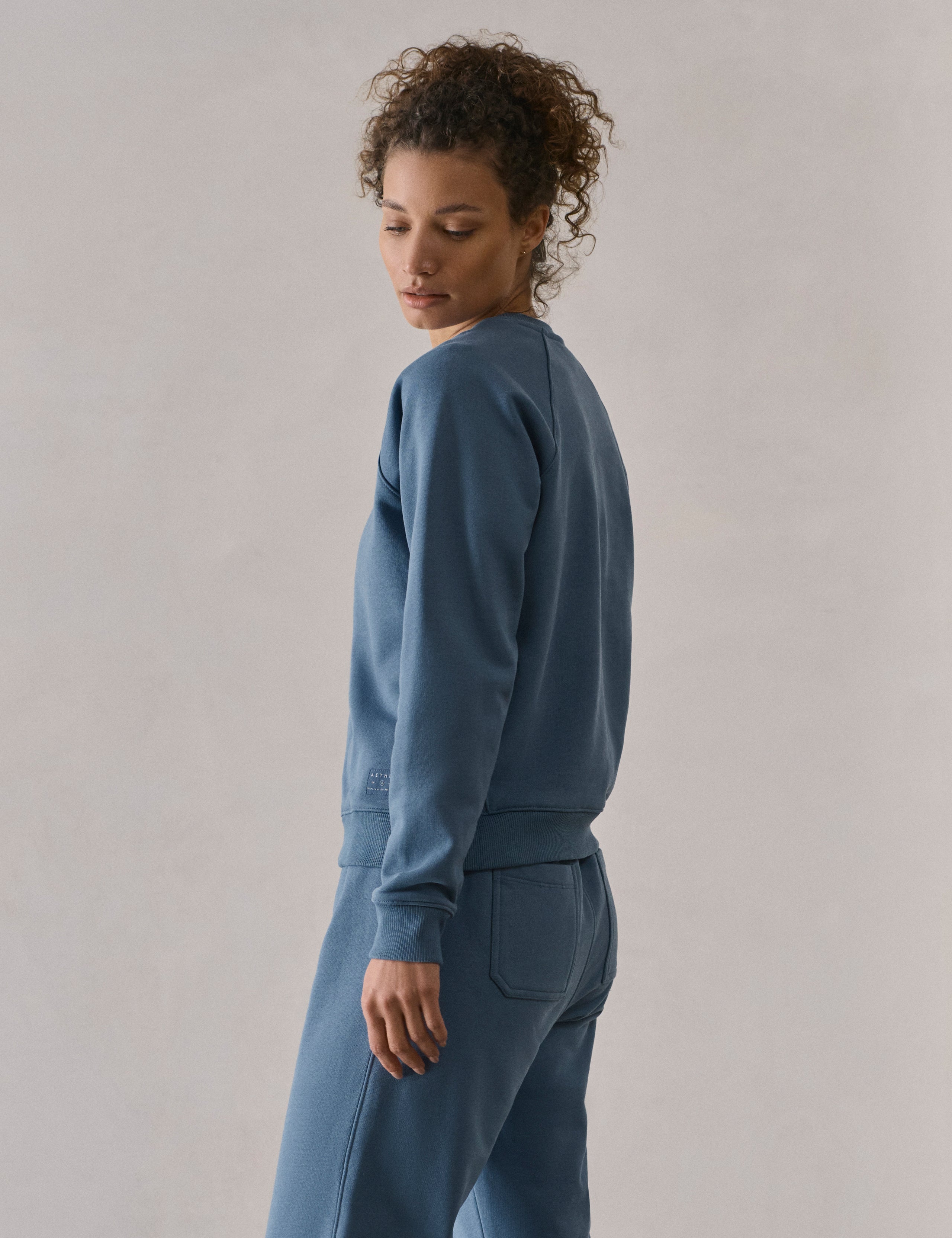 Left side profile upper-body view of woman wearing W Osa Raglan Sweatshirt in Coastal Blue from AETHER Apparel.