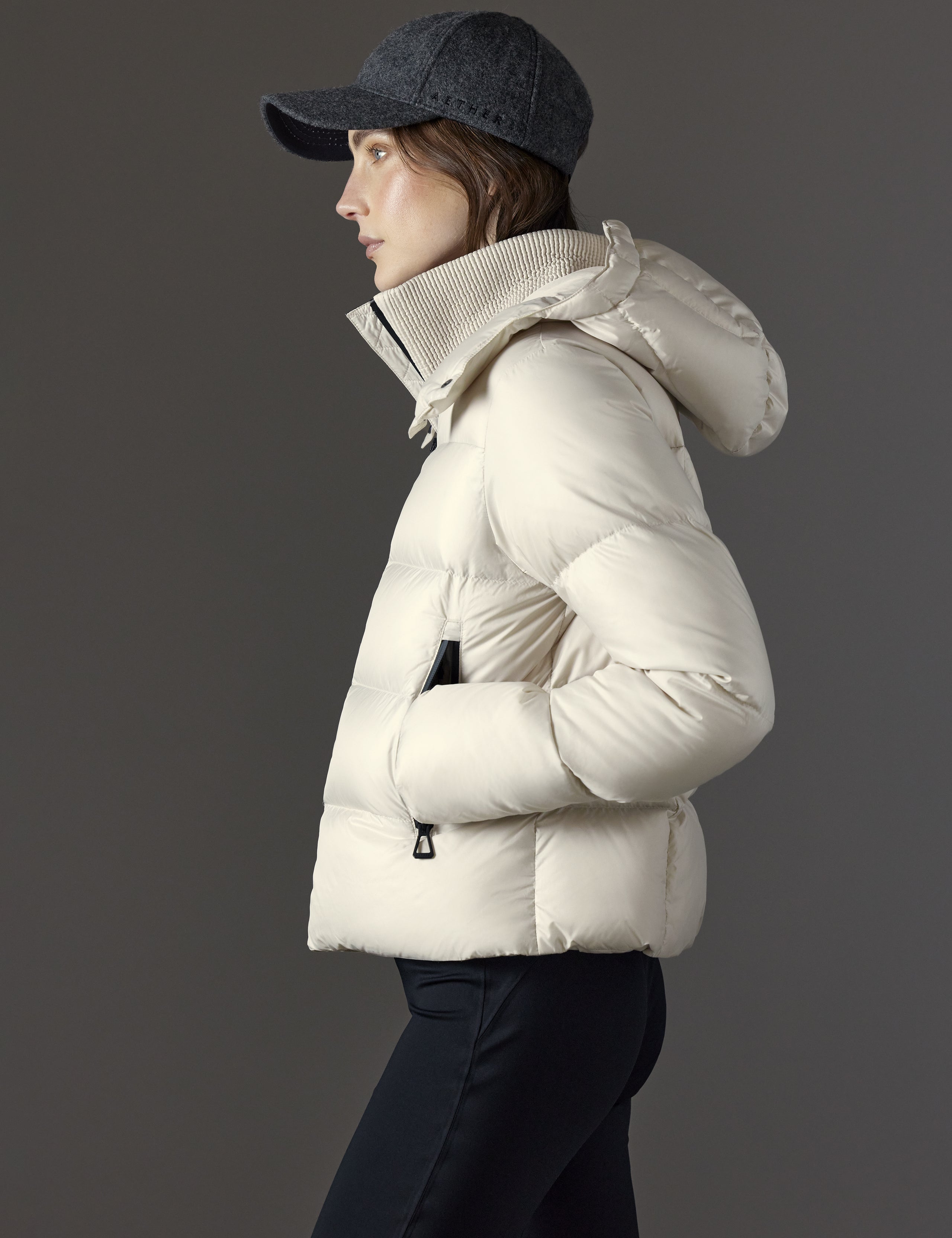 Side profile view of woman wearing Aura Puffer Jacket in Bone white from AETHER Apparel.