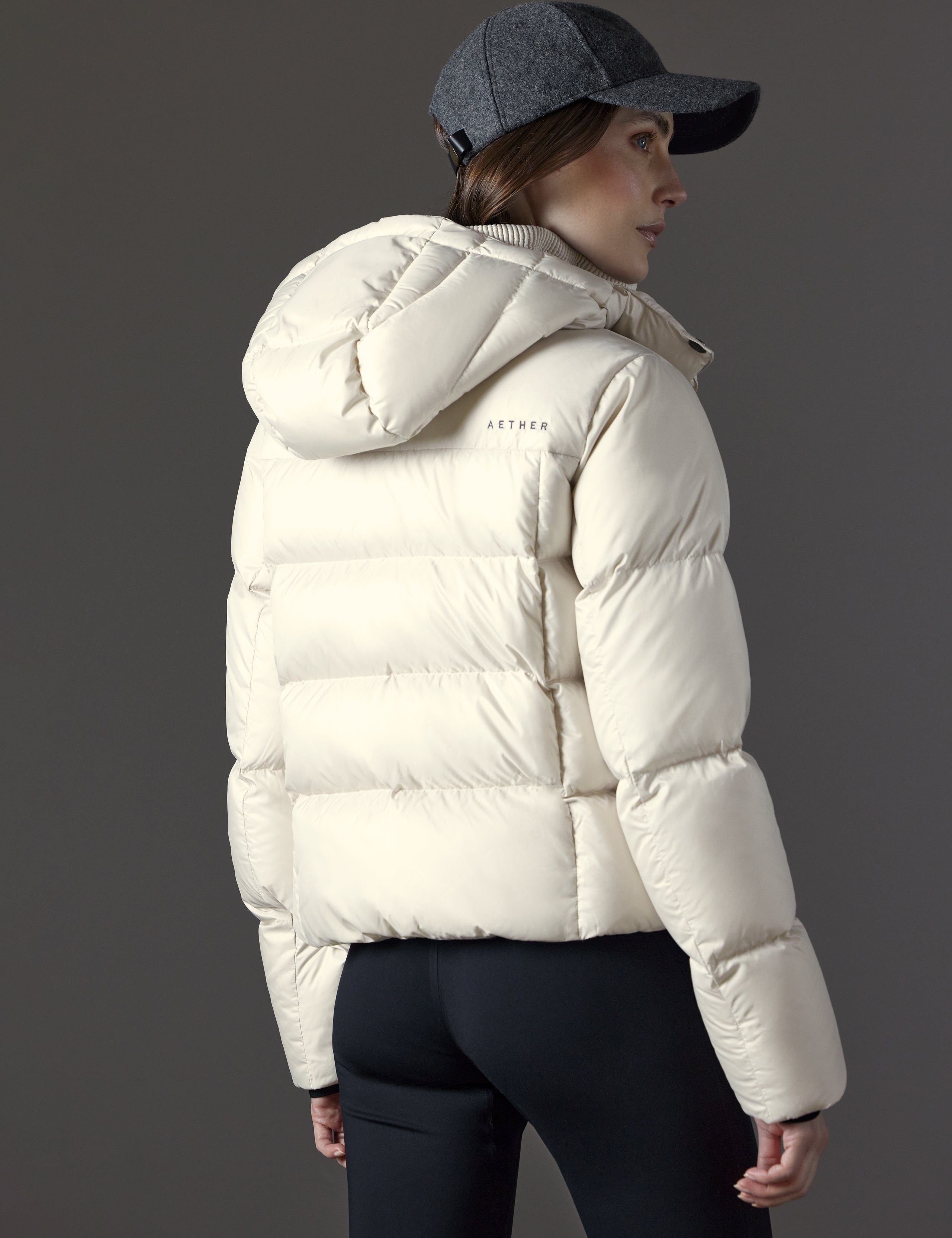Rear angled view of woman wearing Aura Puffer Jacket in Bone white from AETHER Apparel.