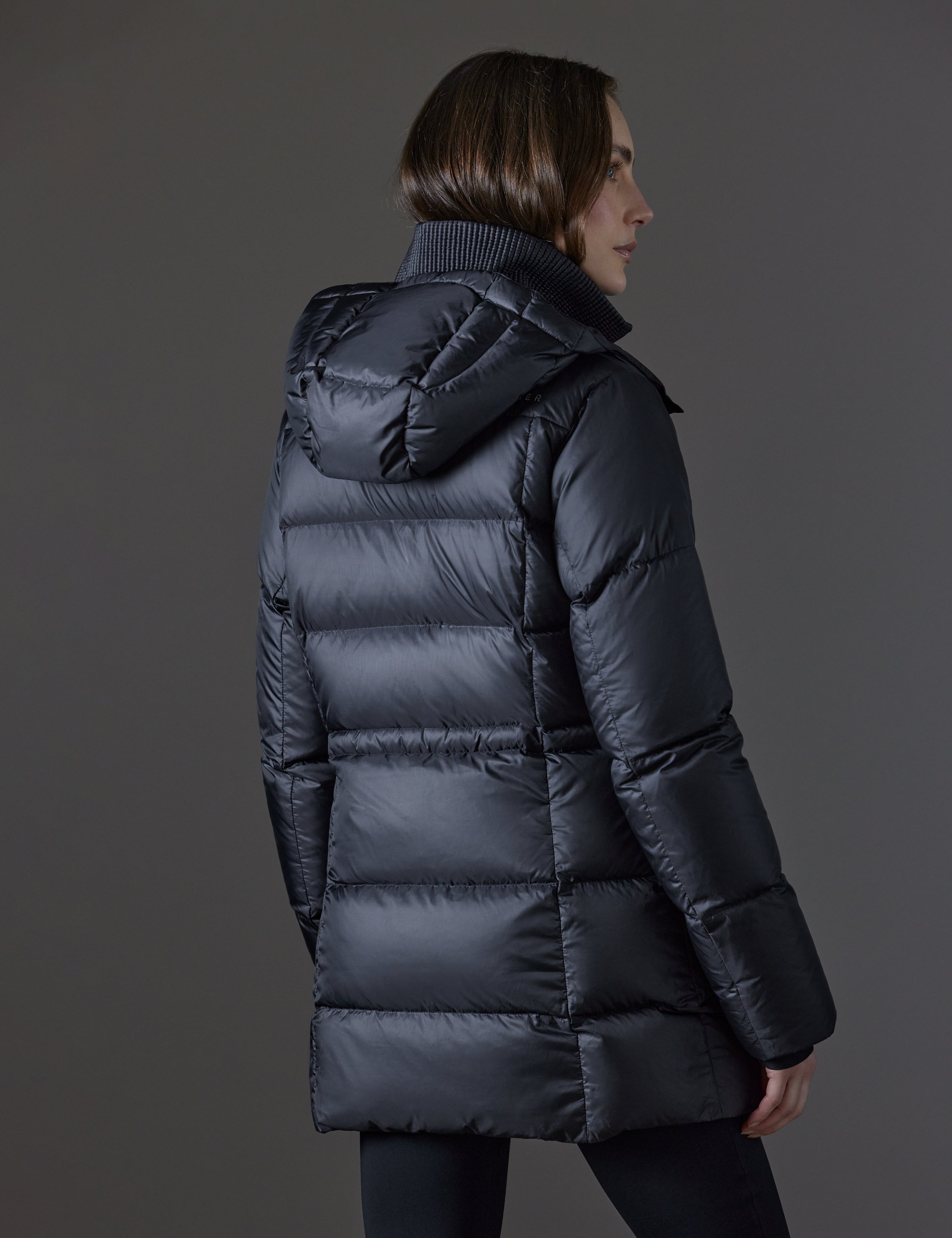 Rear angled view of woman wearing Aura Puffer Long in Onyx Black from AETHER Apparel.