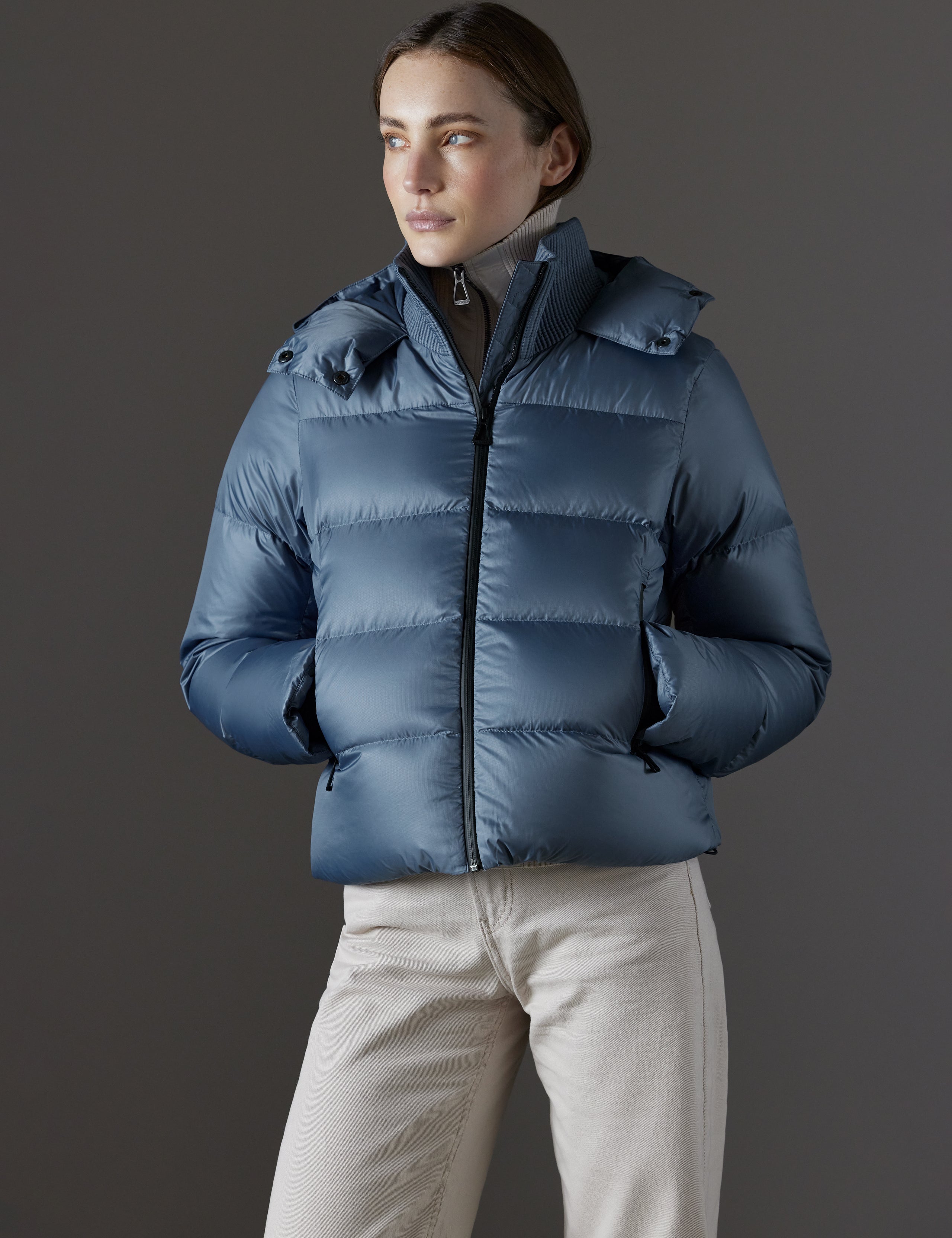 Front view of woman with hands in pockets wearing Aura Puffer Jacket in Portal Blue from AETHER Apparel.