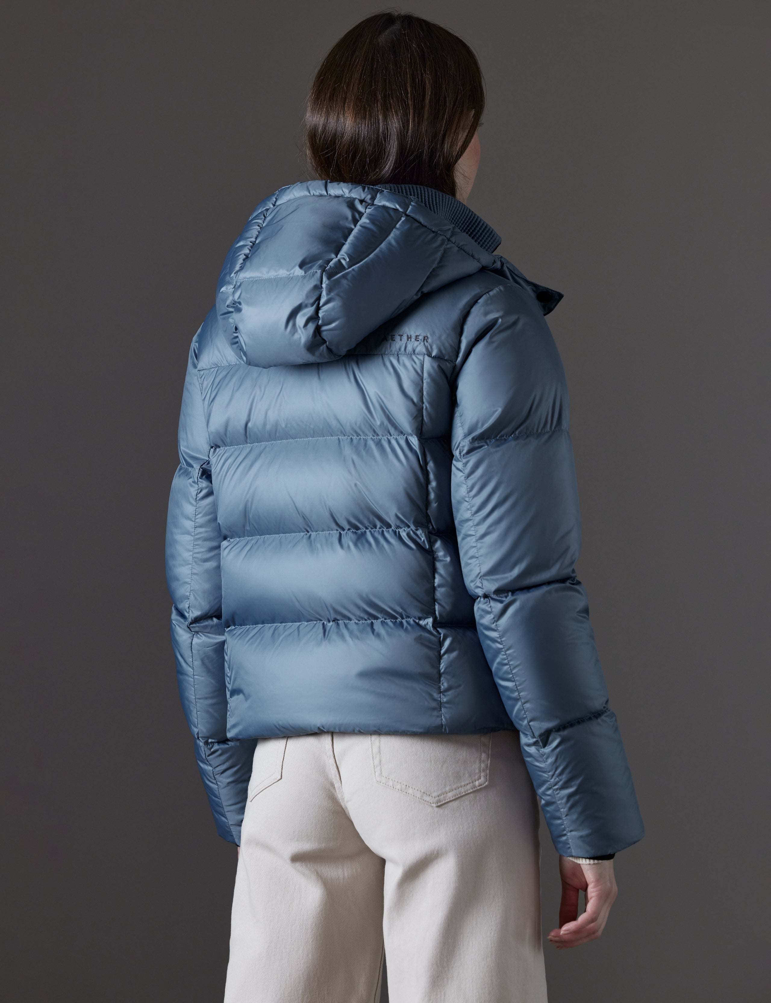 Rear angled view of woman wearing Aura Puffer Jacket in Portal Blue from AETHER Apparel.