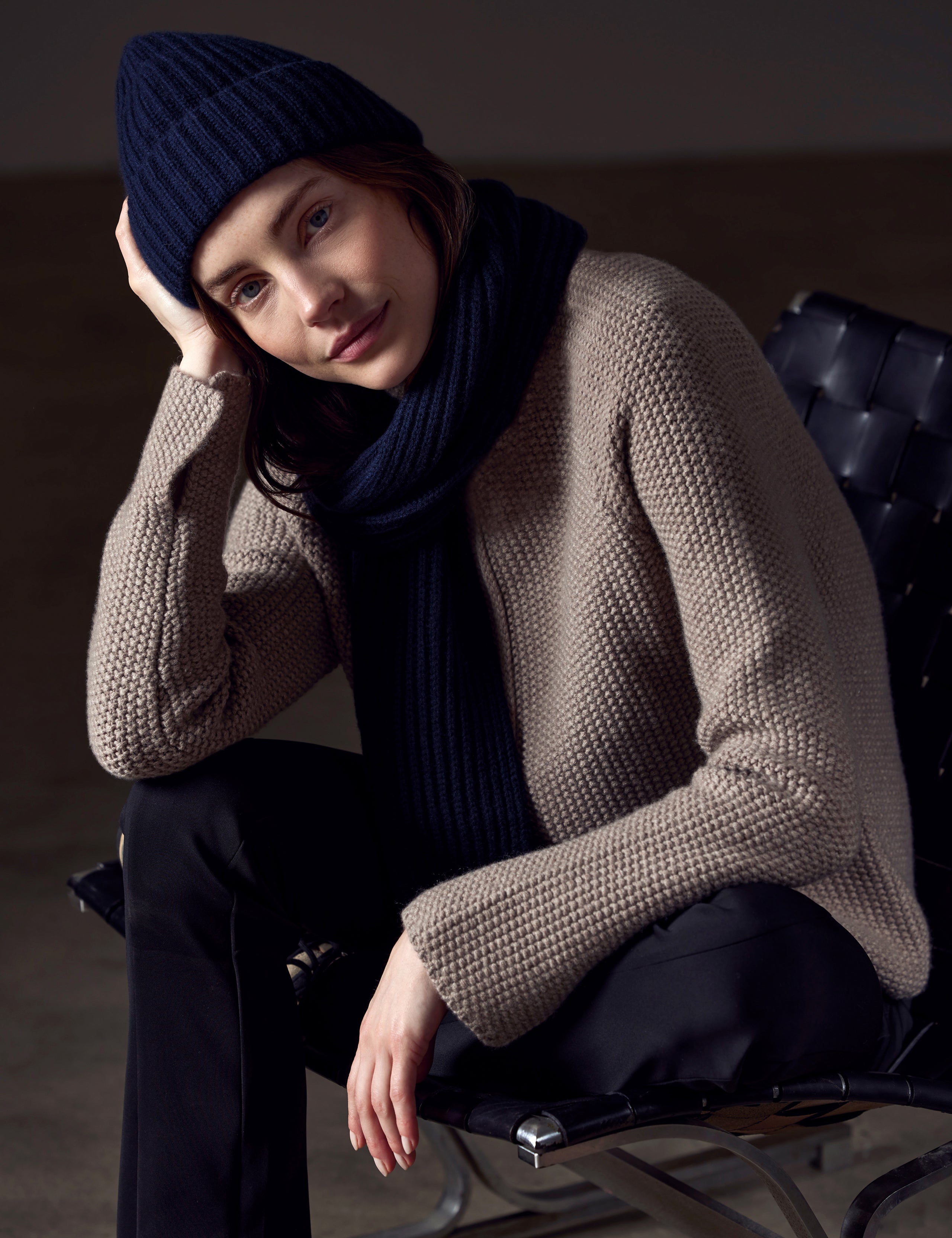 Front angled view of woman sitting in chair wearing Cashmere Scarf and Cashmere Hat in Total Eclipse Dark Blue from AETHER Apparel. 
