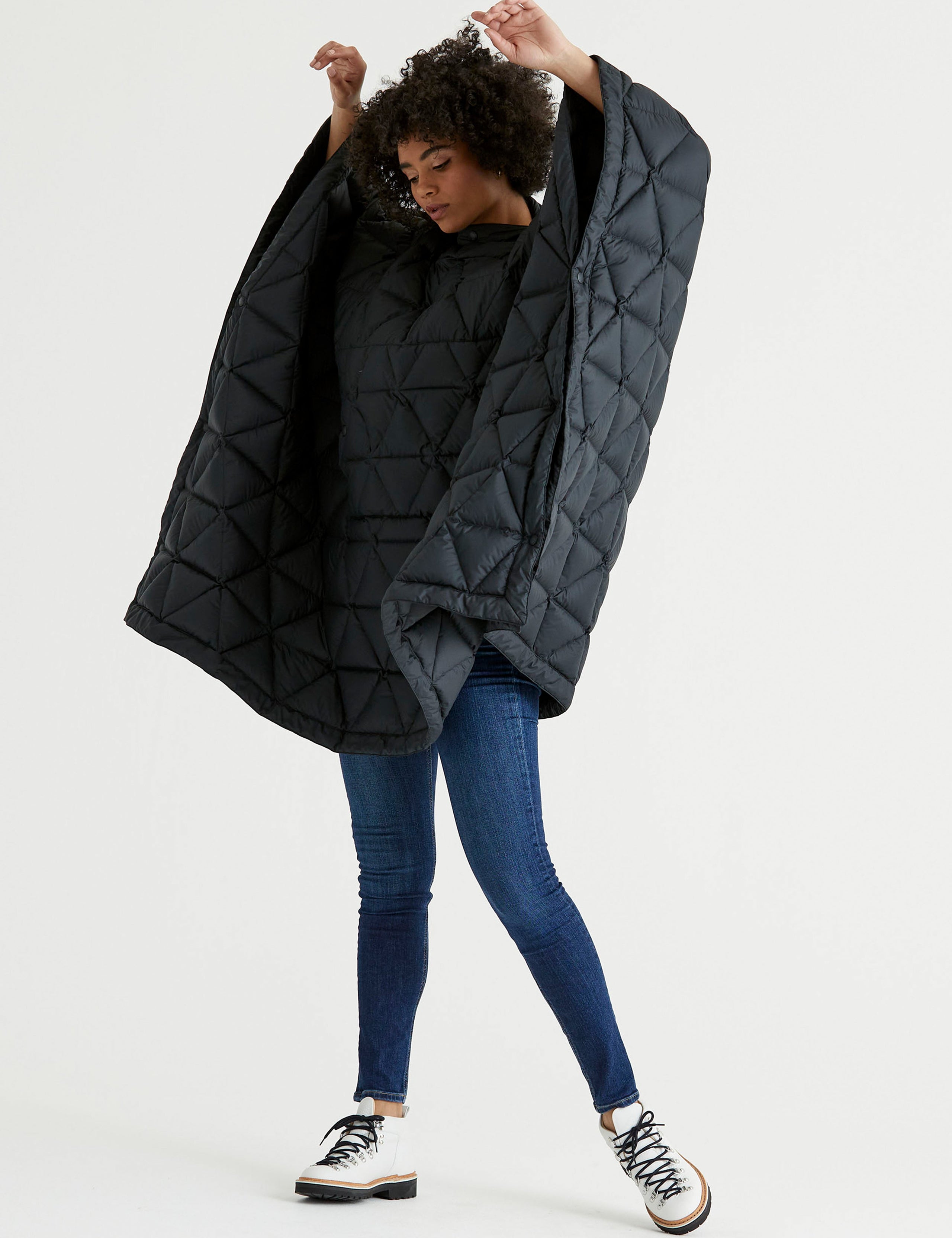 Front 3/4 full-body view of woman raising arms wearing Down Poncho in Onyx Black from AETHER Apparel.