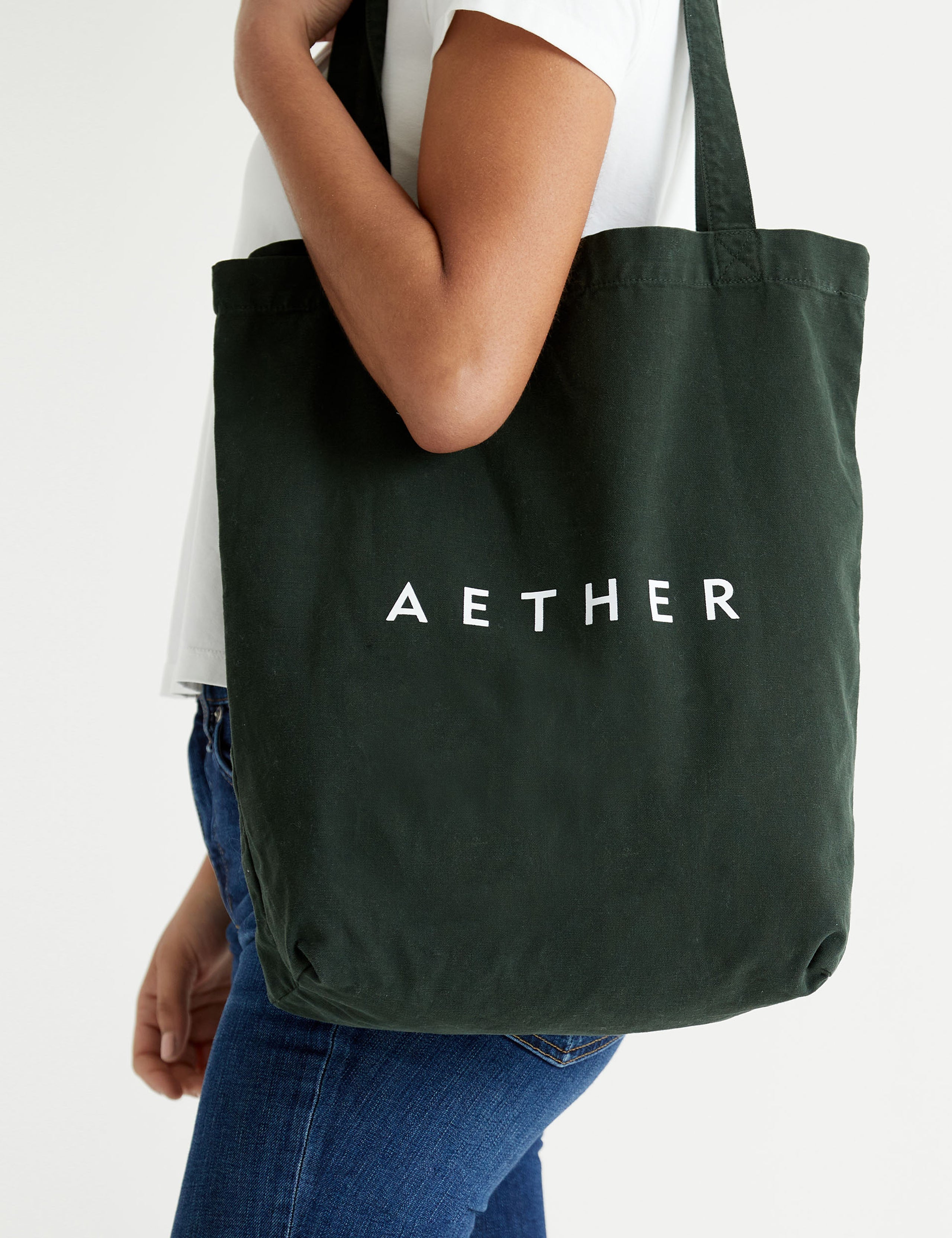 Side profile view of woman carrying Lifestyle Canvas Tote in Duffle Green from AETHER Apparel over shoulder.