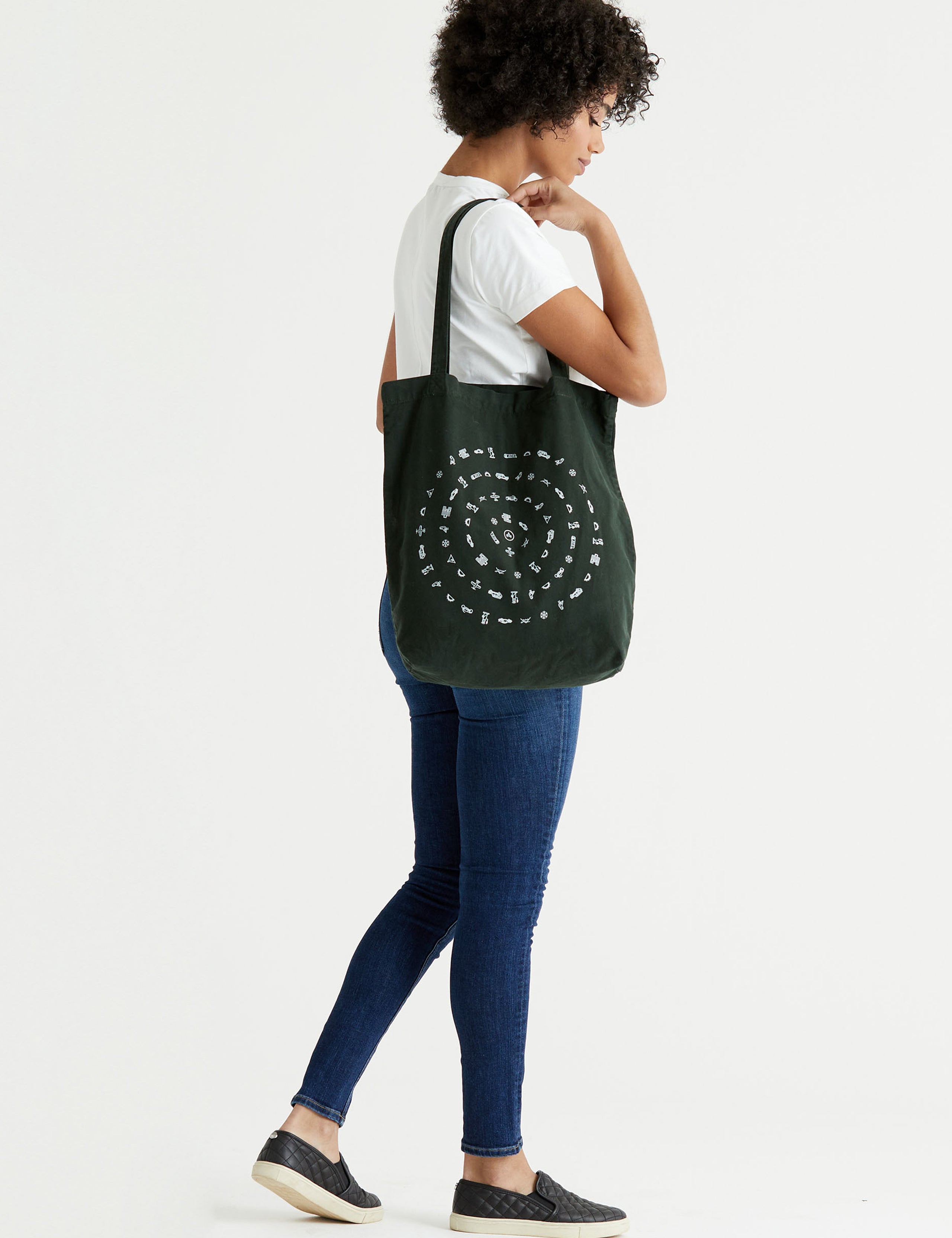 Side profile full-body view of woman carrying Lifestyle Canvas Tote in Duffle Green from AETHER Apparel over shoulder.