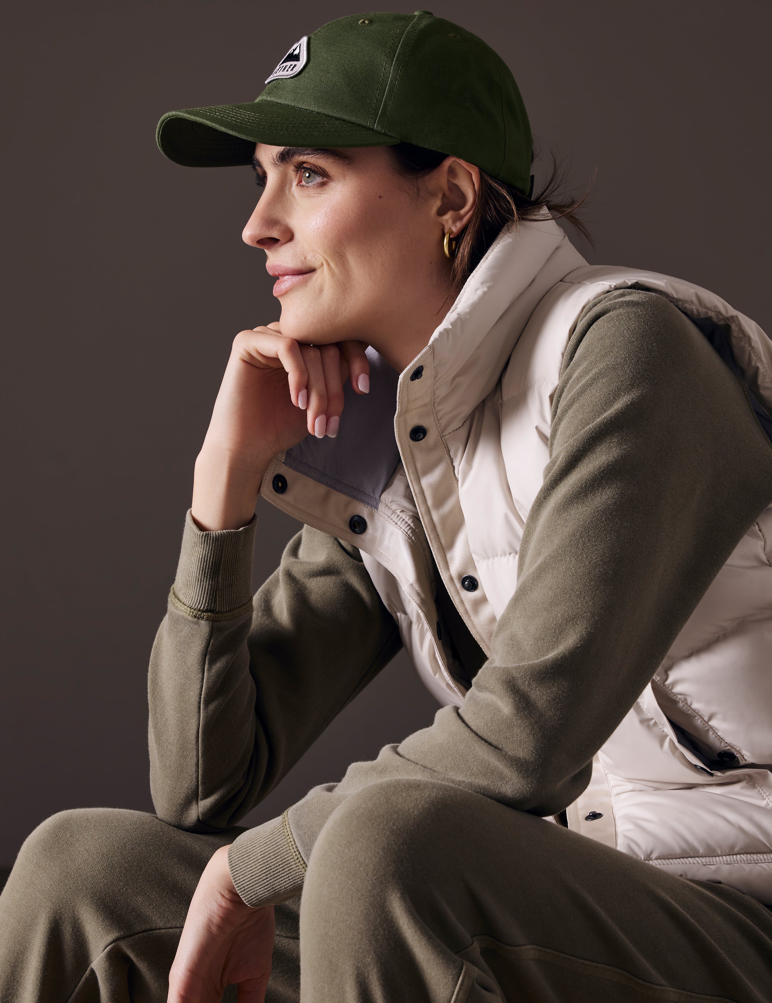 Side profile view of woman sitting wearing AETHER Mountain Hat in Army Green from AETHER Apparel.