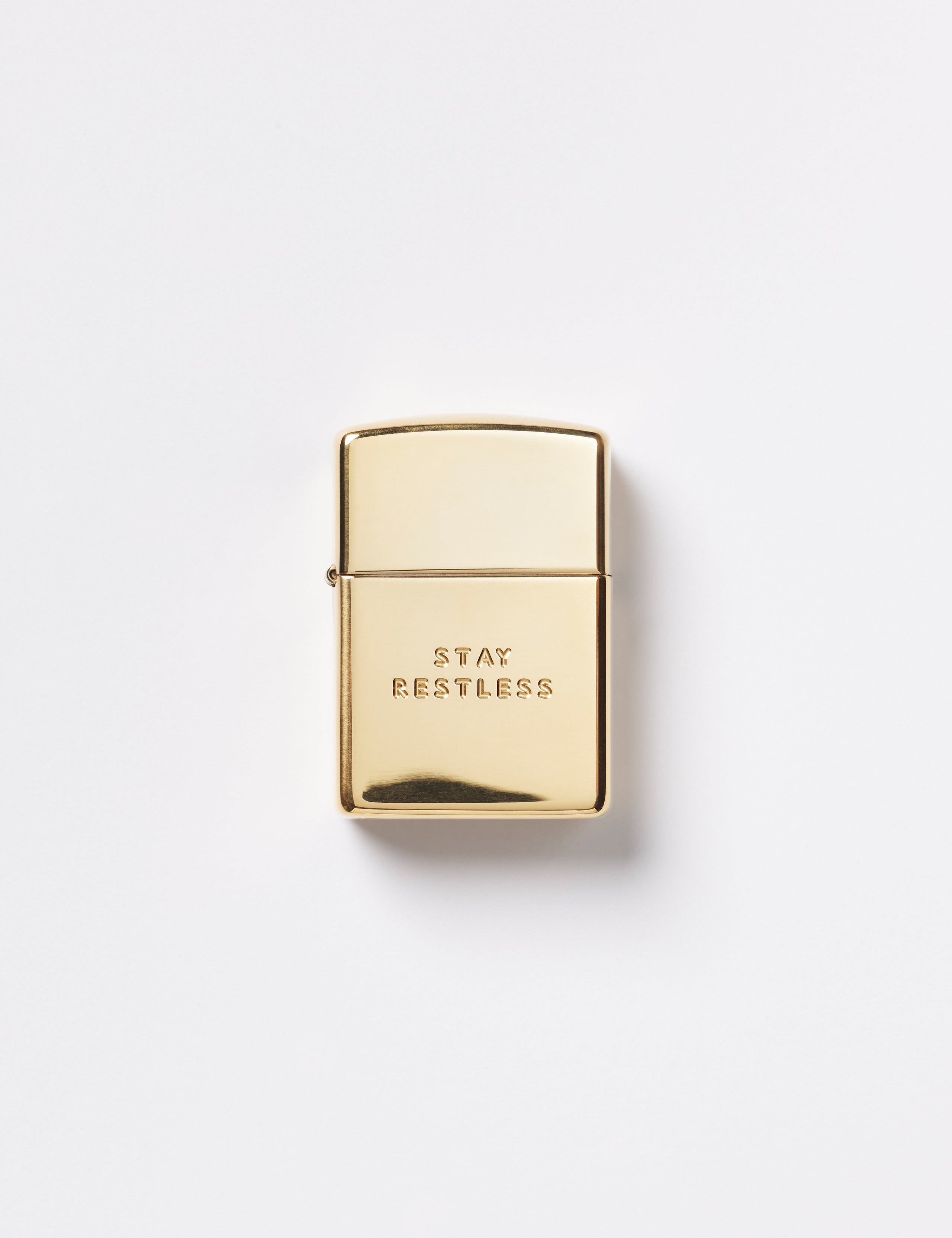 Flay lay view of front of Restless Zippo Lighter in high polish brass from AETHER Apparel with top closed. 