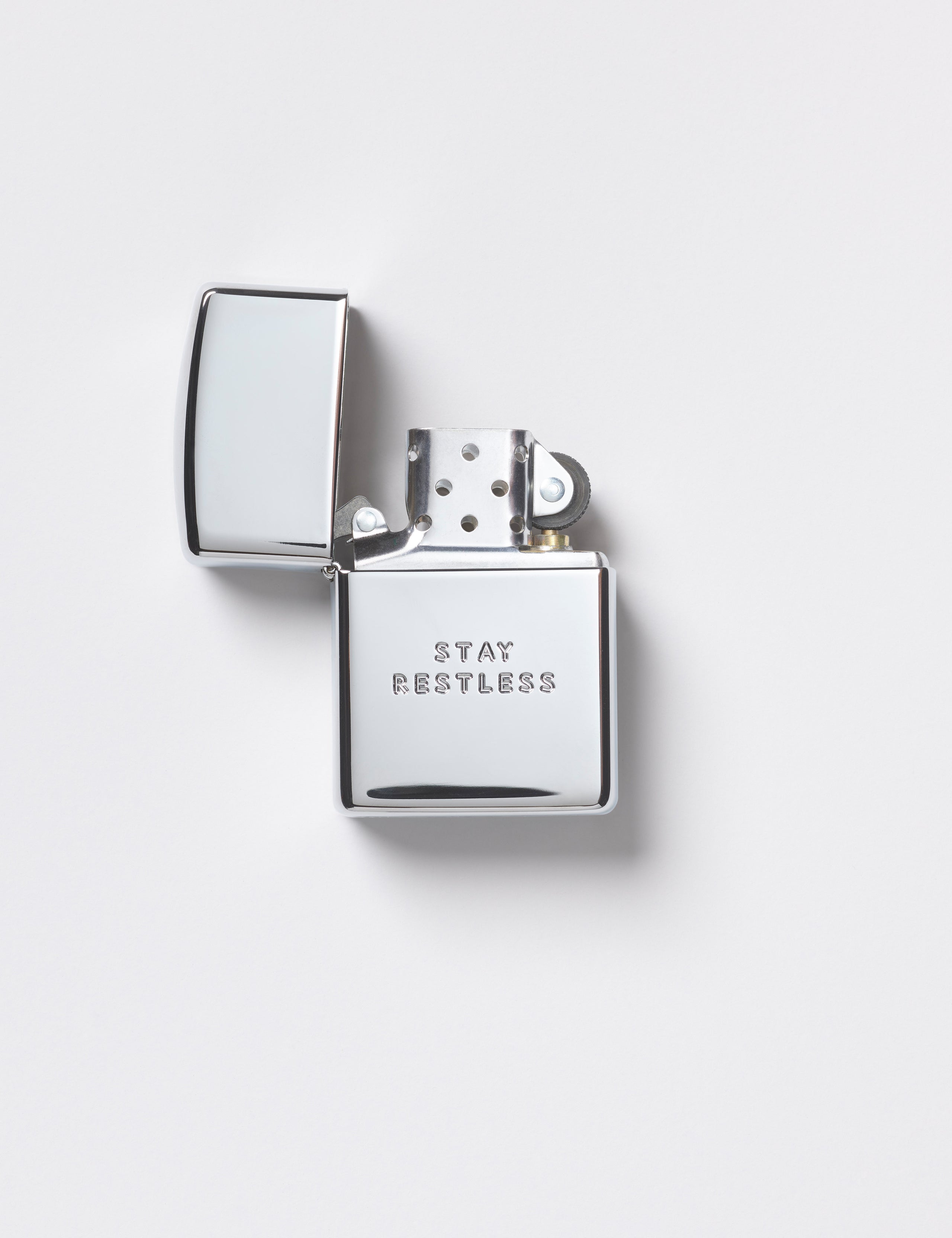Flay lay view of front of Restless Zippo Lighter in high polish chrome from AETHER Apparel with top open. 