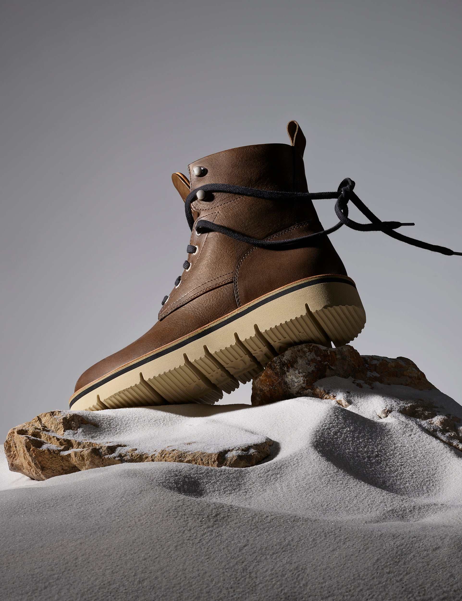 Studio image of Canyon Boot in Cedar Brown from AETHER Apparel on rocks and sand. 