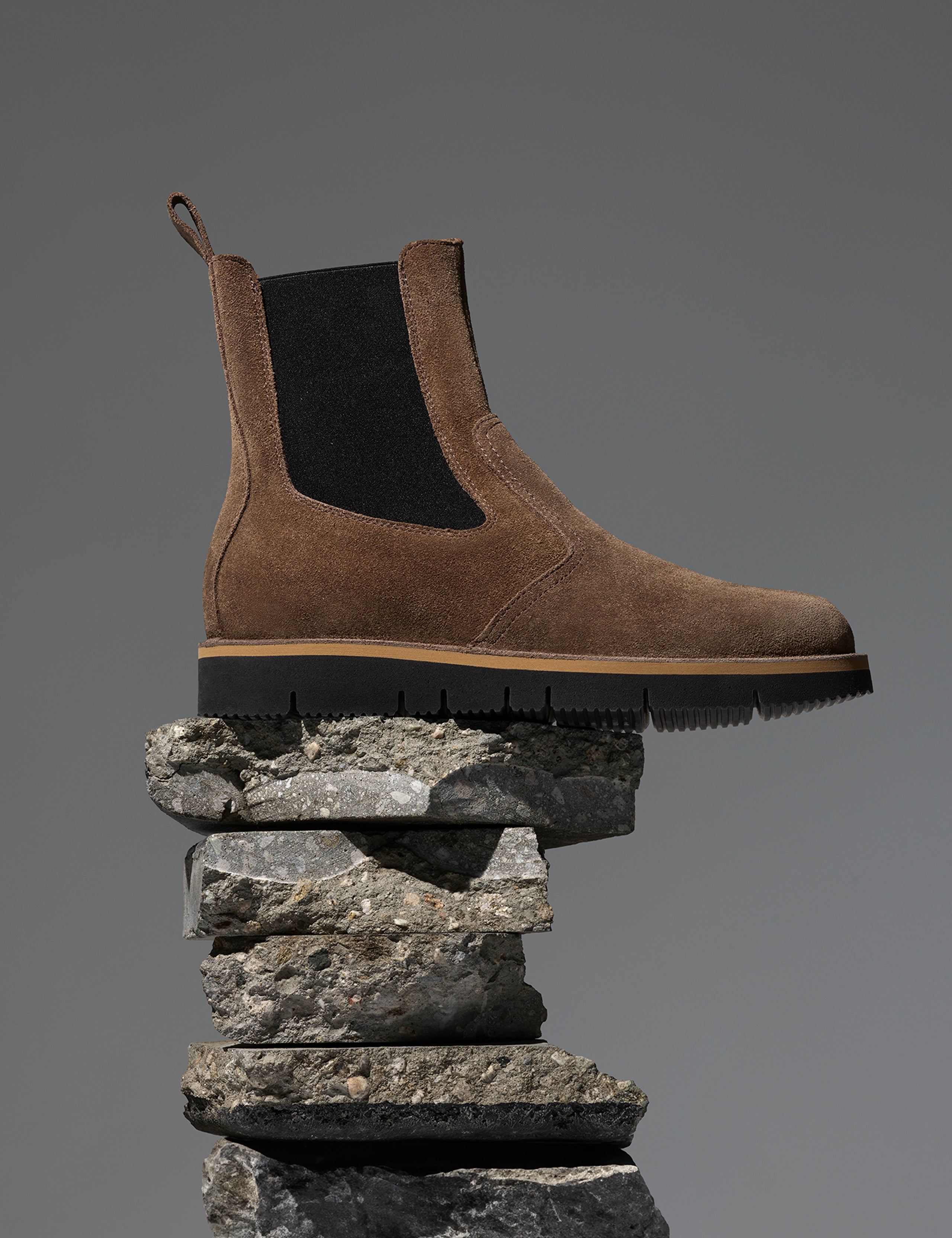 Studio side profile image of AETHER Chelsea Boot in Taupe from AETHER Apparel on pile of rocks. 