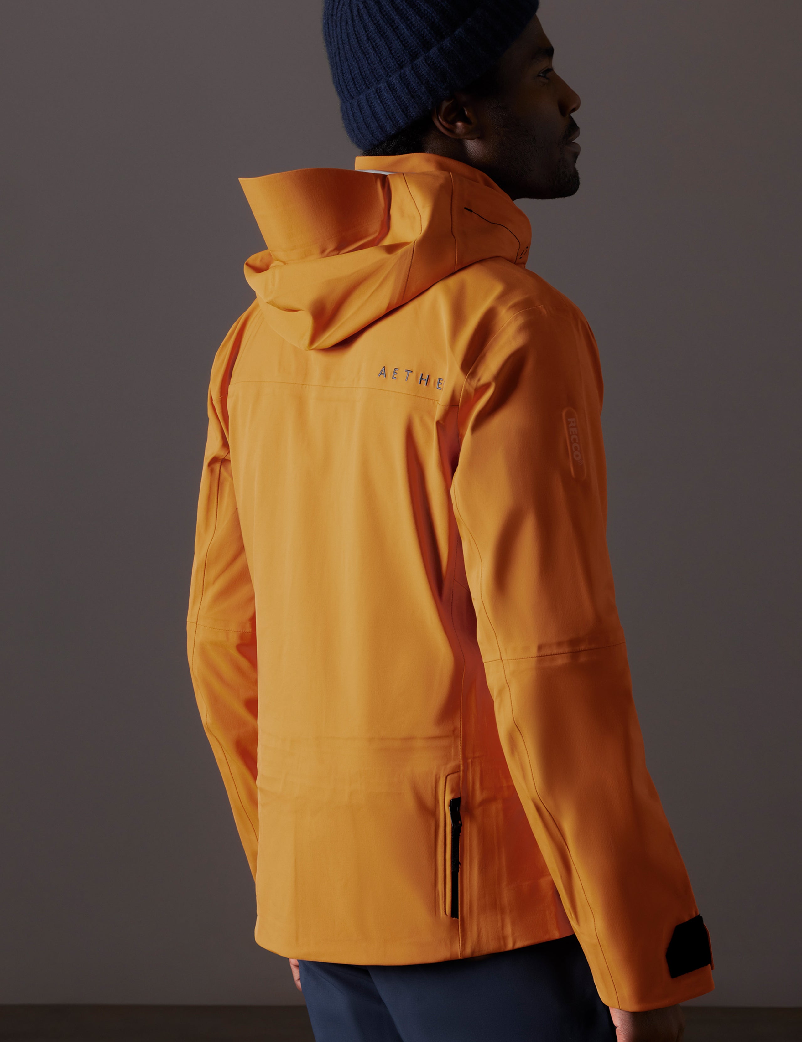 Rear 3/4 body view of man wearing Altitude Snow Shell 2.0 in Autumn Orange from AETHER Apparel.