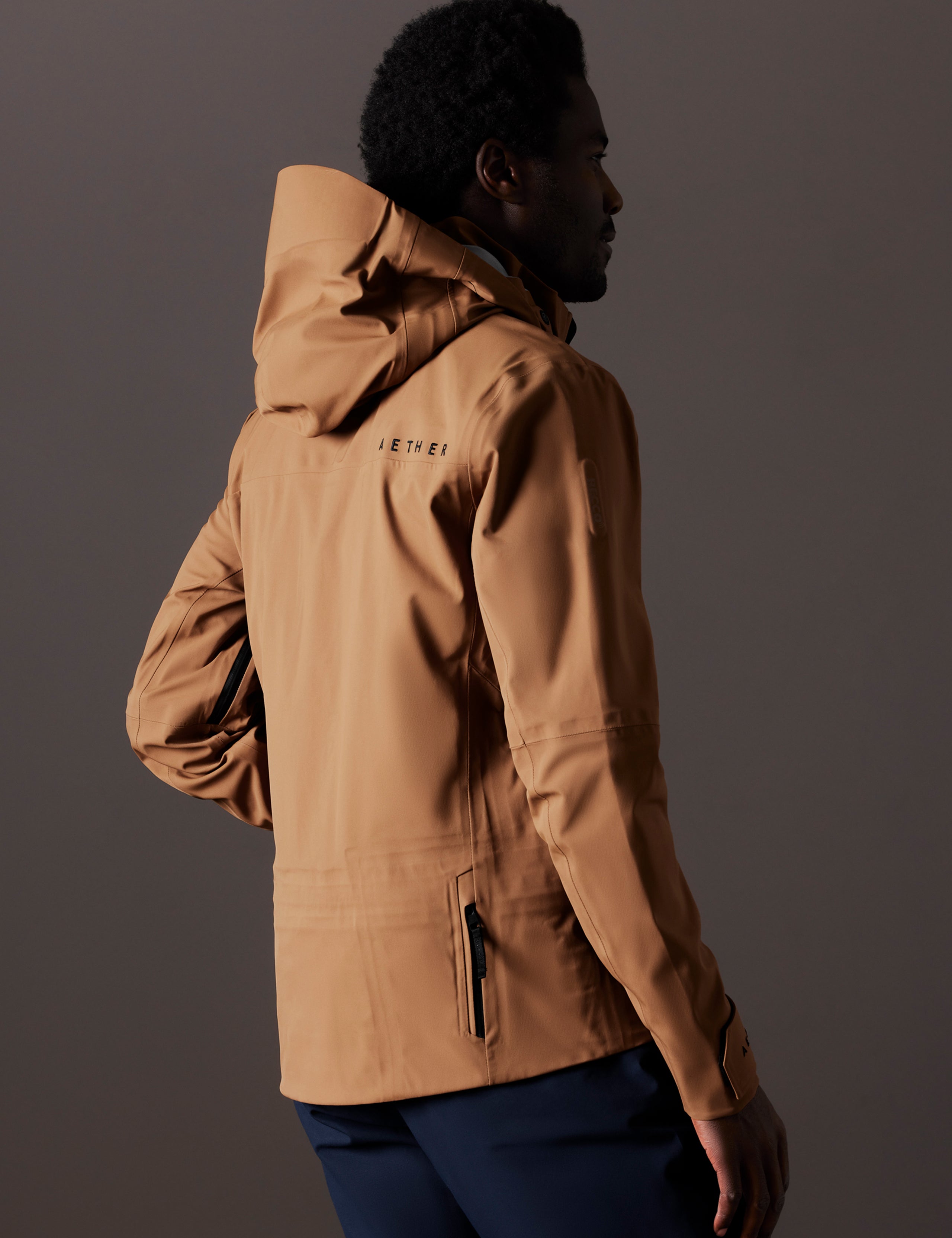 Rear 3/4 body view of man wearing Altitude Snow Shell 2.0 in Rubber Brown from AETHER Apparel.