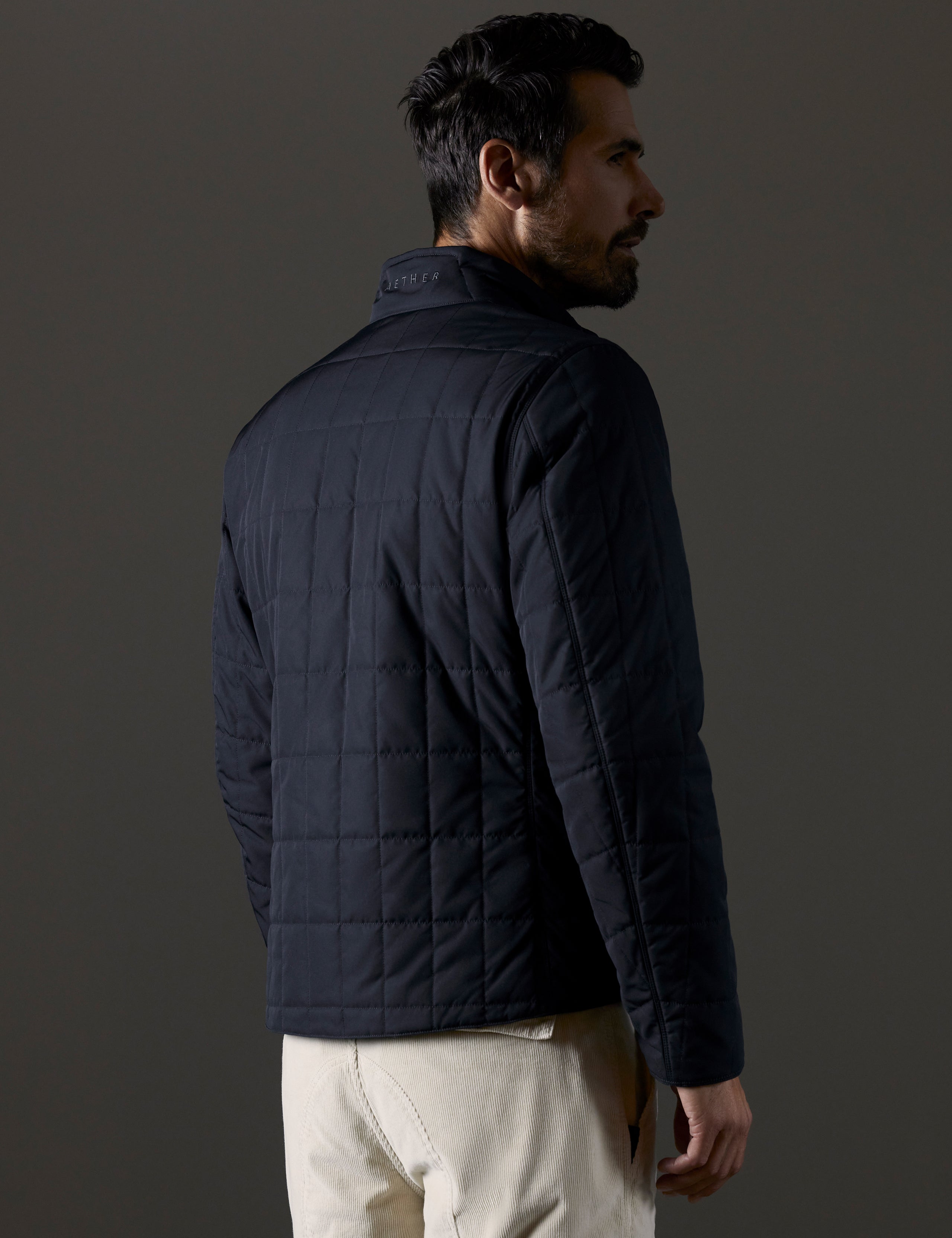 Rear 3/4 body view of man wearing Alto Jacket in Onyx Black from AETHER Apparel.