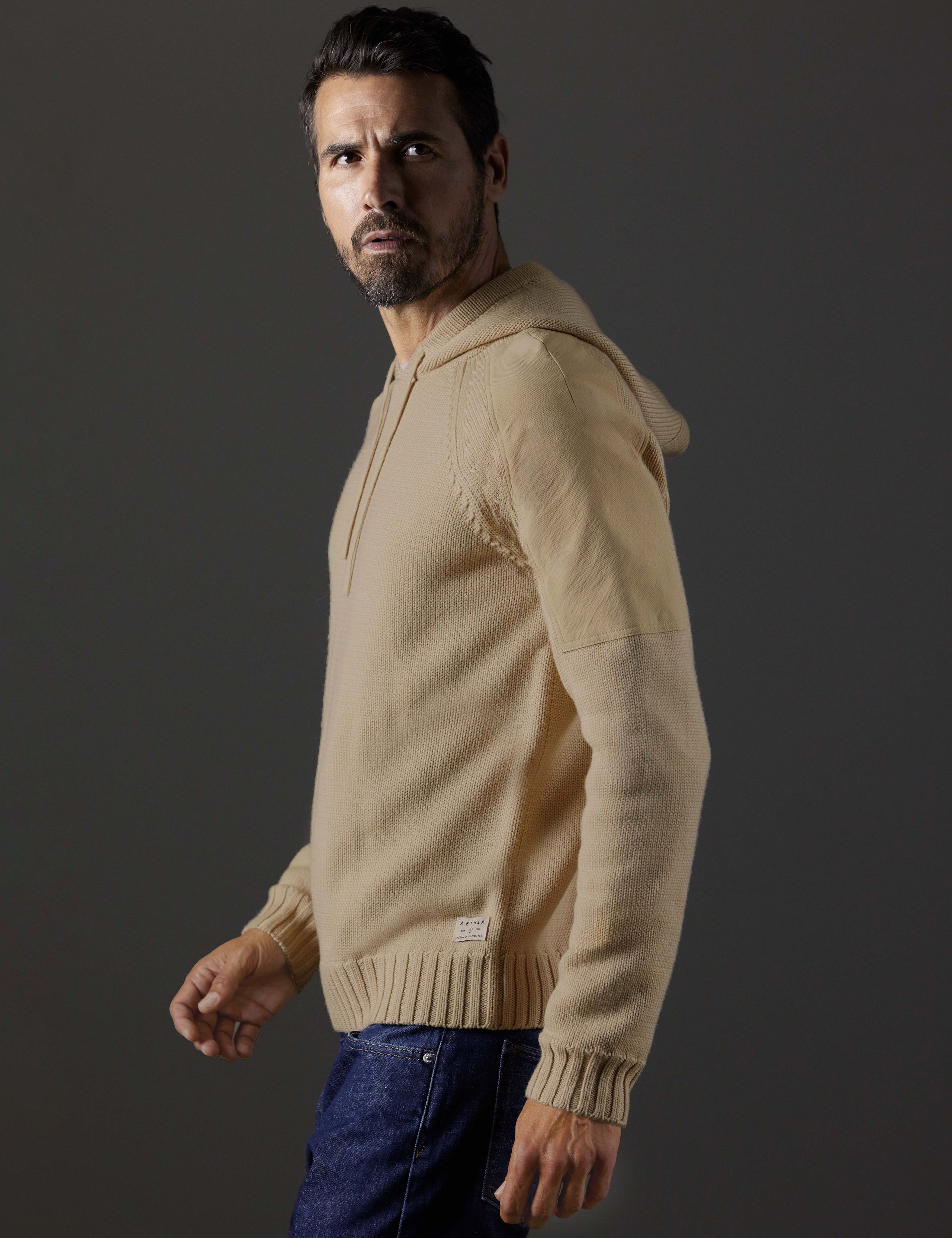Side profile body view of man wearing Benson Hooded Sweater in Oatmeal beige from AETHER Apparel.