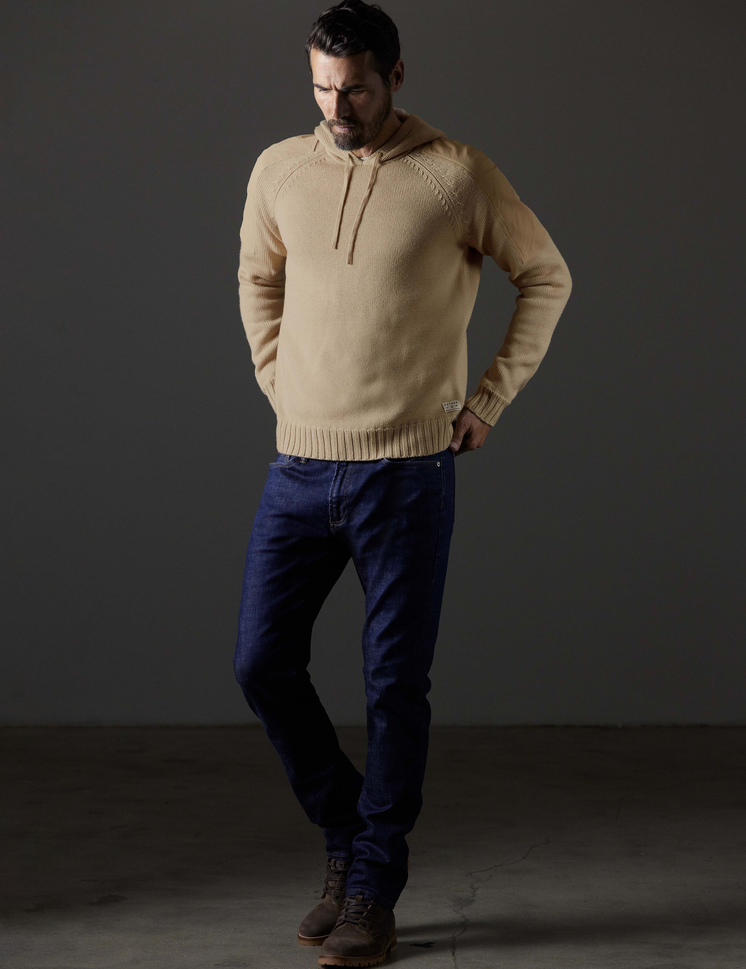 Front 3/4 full-body view of man wearing Benson Hooded Sweater in Oatmeal beige from AETHER Apparel.