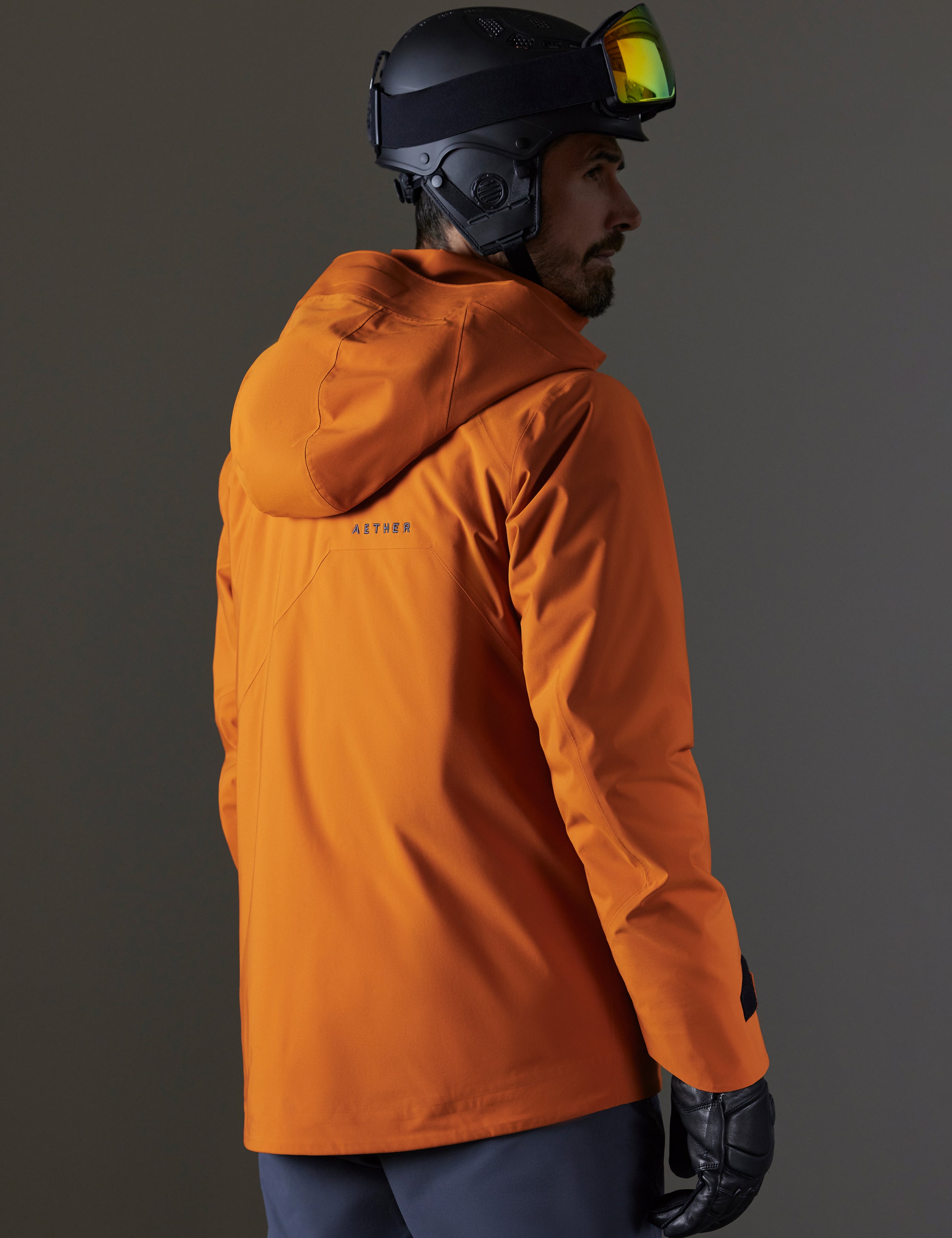 Rear 3/4 body view of man wearing Brighton Insulated Snow Jacket in Autumn Orange from AETHER Apparel.