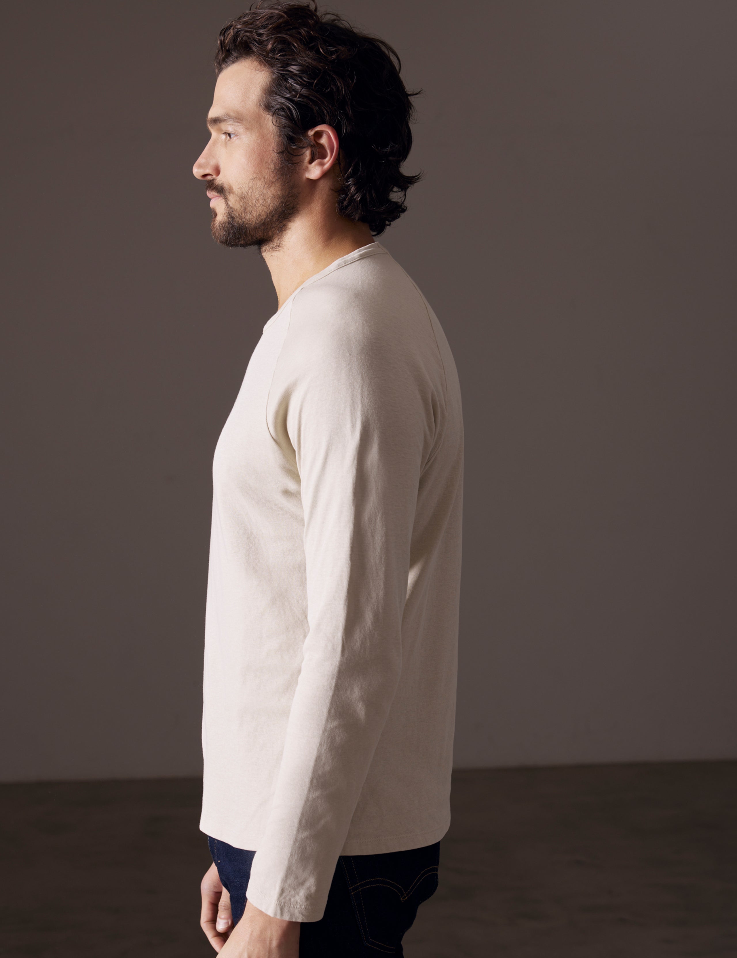 Side profile body view of man wearing Buckhorn Cotton Raglan Long-Sleeve Tee in Bone white from AETHER Apparel.