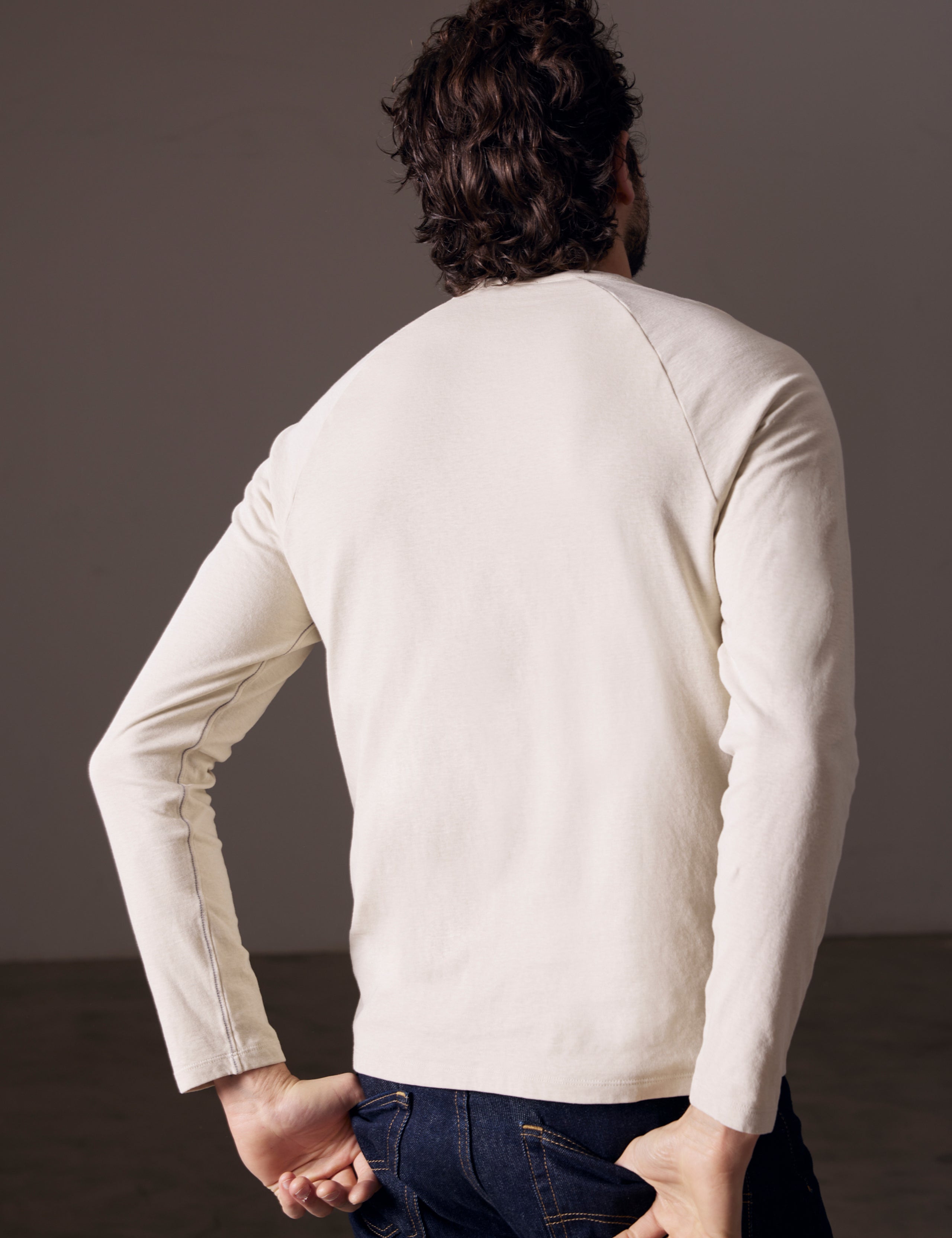 Rear angled body view of man wearing Buckhorn Cotton Raglan Long-Sleeve Tee in Bone white from AETHER Apparel.