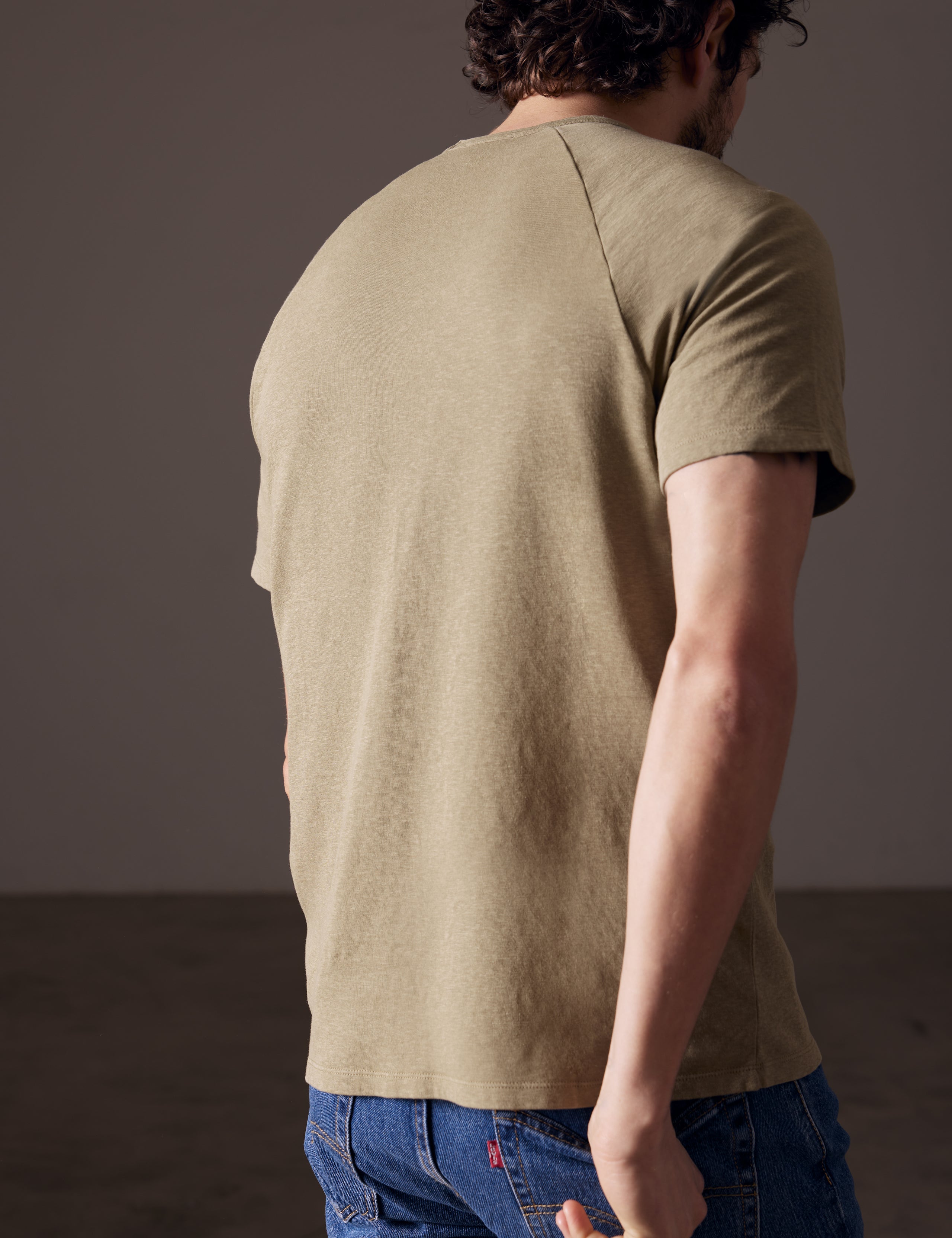Rear angled body view of man wearing Buckhorn Cotton Raglan Tee in Mineral Green from AETHER Apparel.