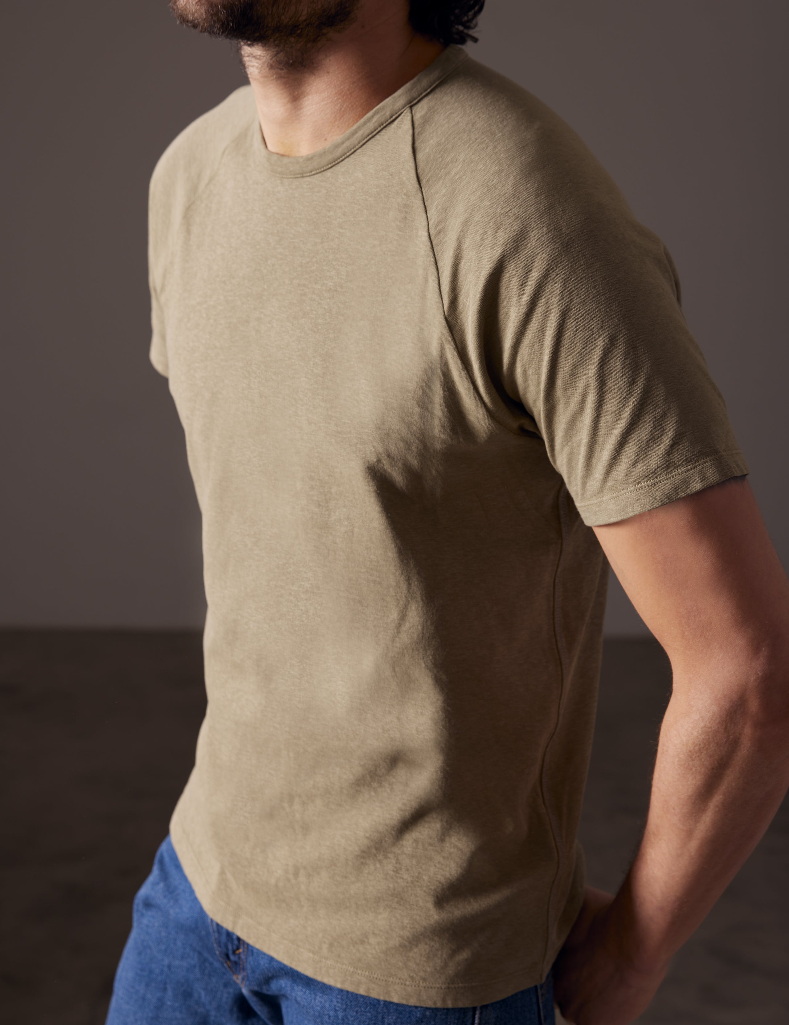 Angled closeup view of man wearing Buckhorn Cotton Raglan Tee in Mineral Green from AETHER Apparel.