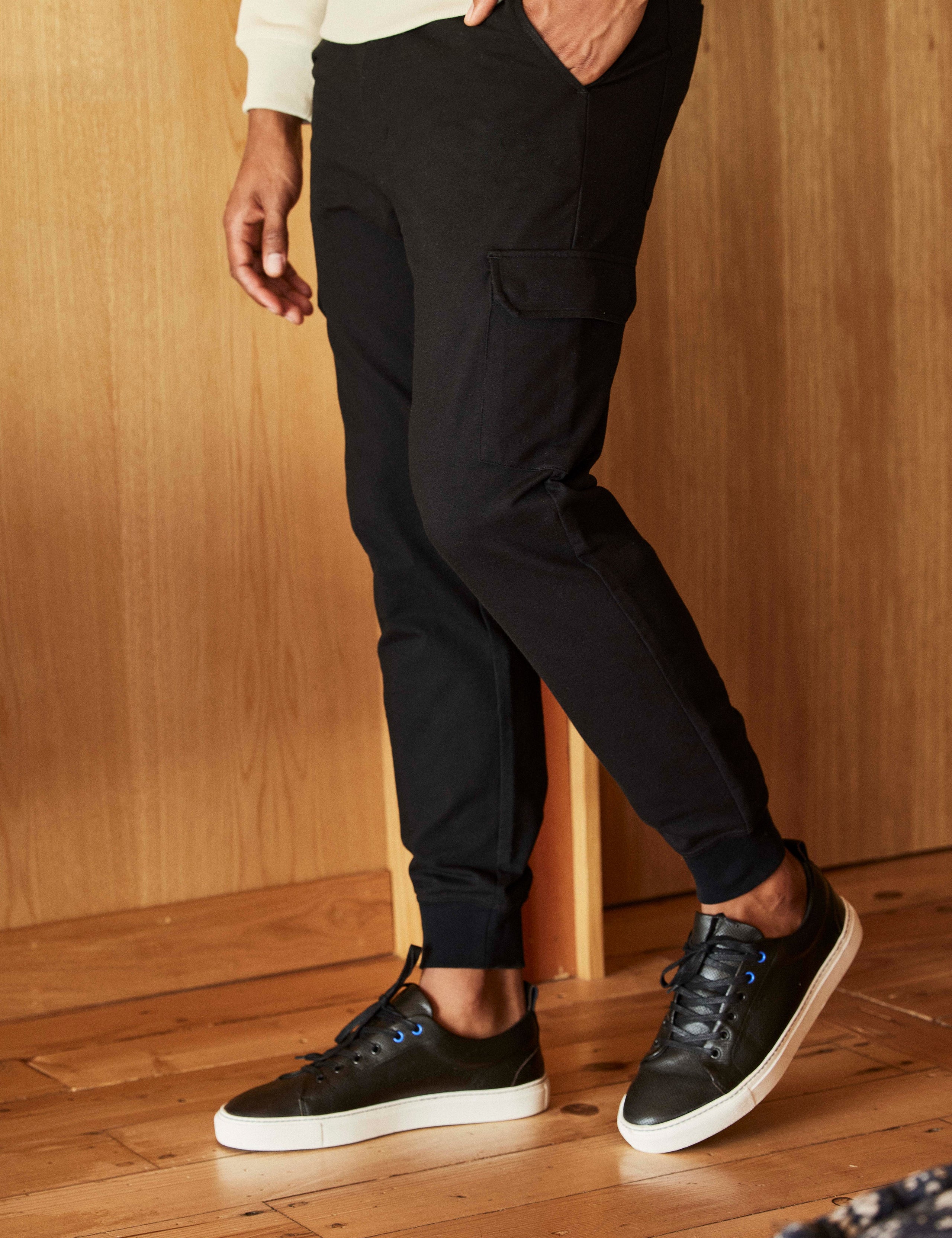 Lifestyle image of man standing on wood floor wearing Dalton Low-Top Sneaker in Onyx Black from AETHER Apparel.