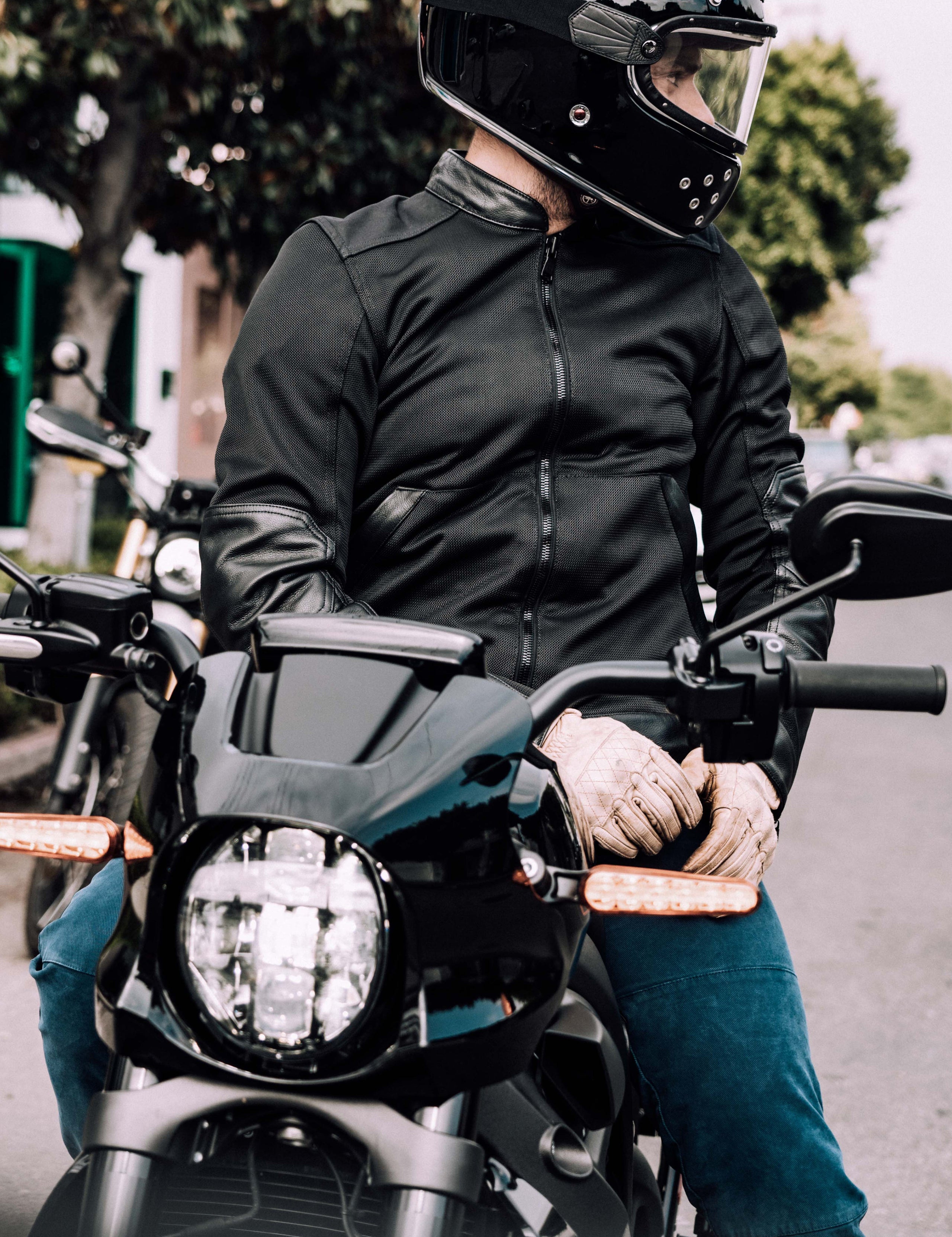 Outdoor lifestyle image of man sitting on motorcycle wearing Draft Mesh Motorcycle Jacket in Jet Black from AETHER Apparel.