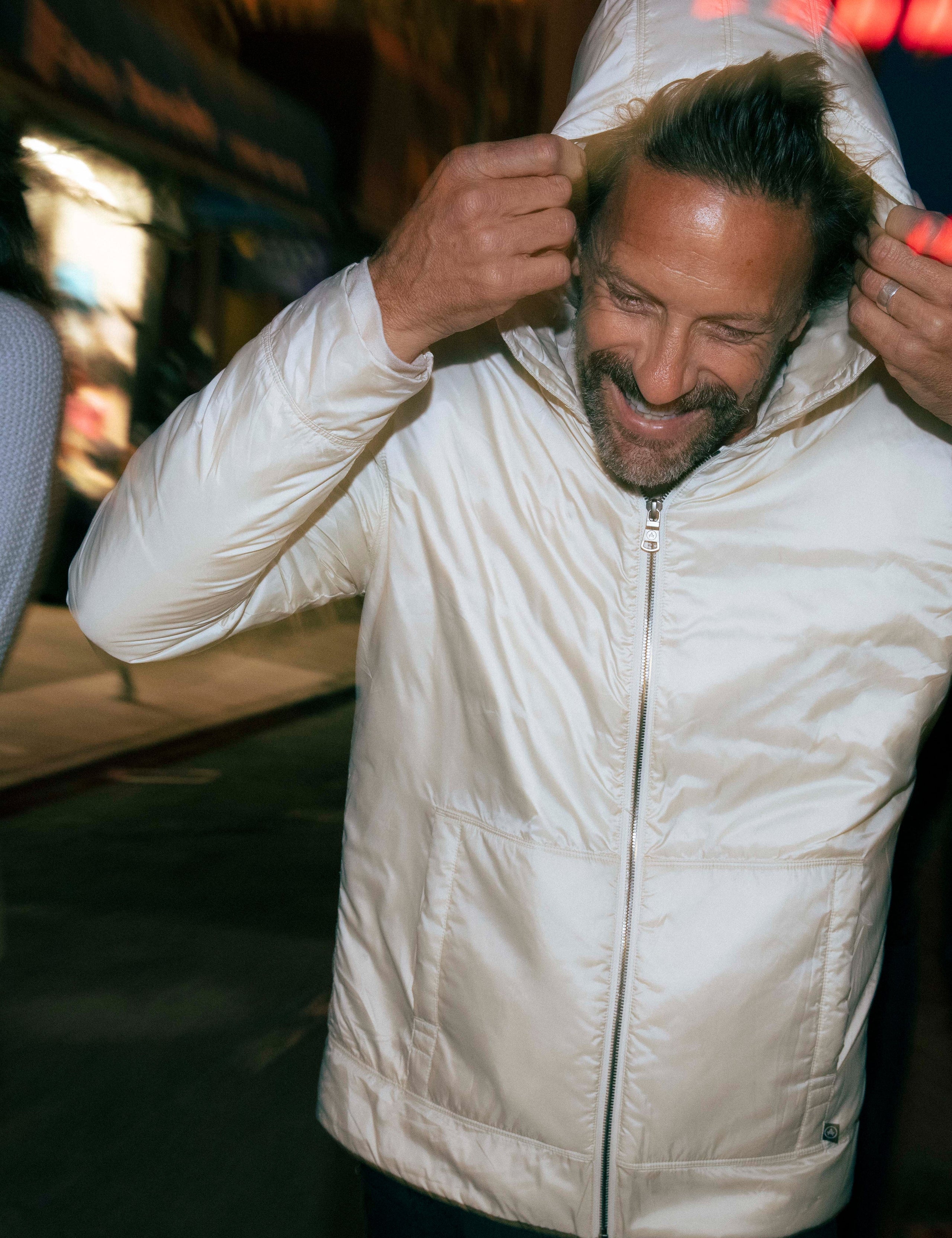 Outdoor lifestyle image of man putting on hood of Eco Space Hoodie in Winter White from AETHER Apparel.