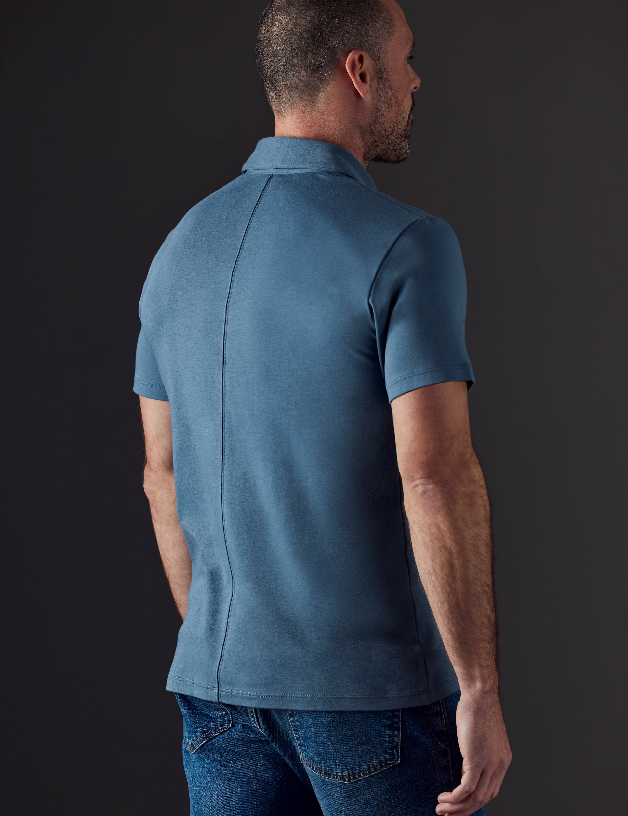 Rear 3/4 body view of man wearing Emery Pima Polo in Coastal Blue from AETHER Apparel.