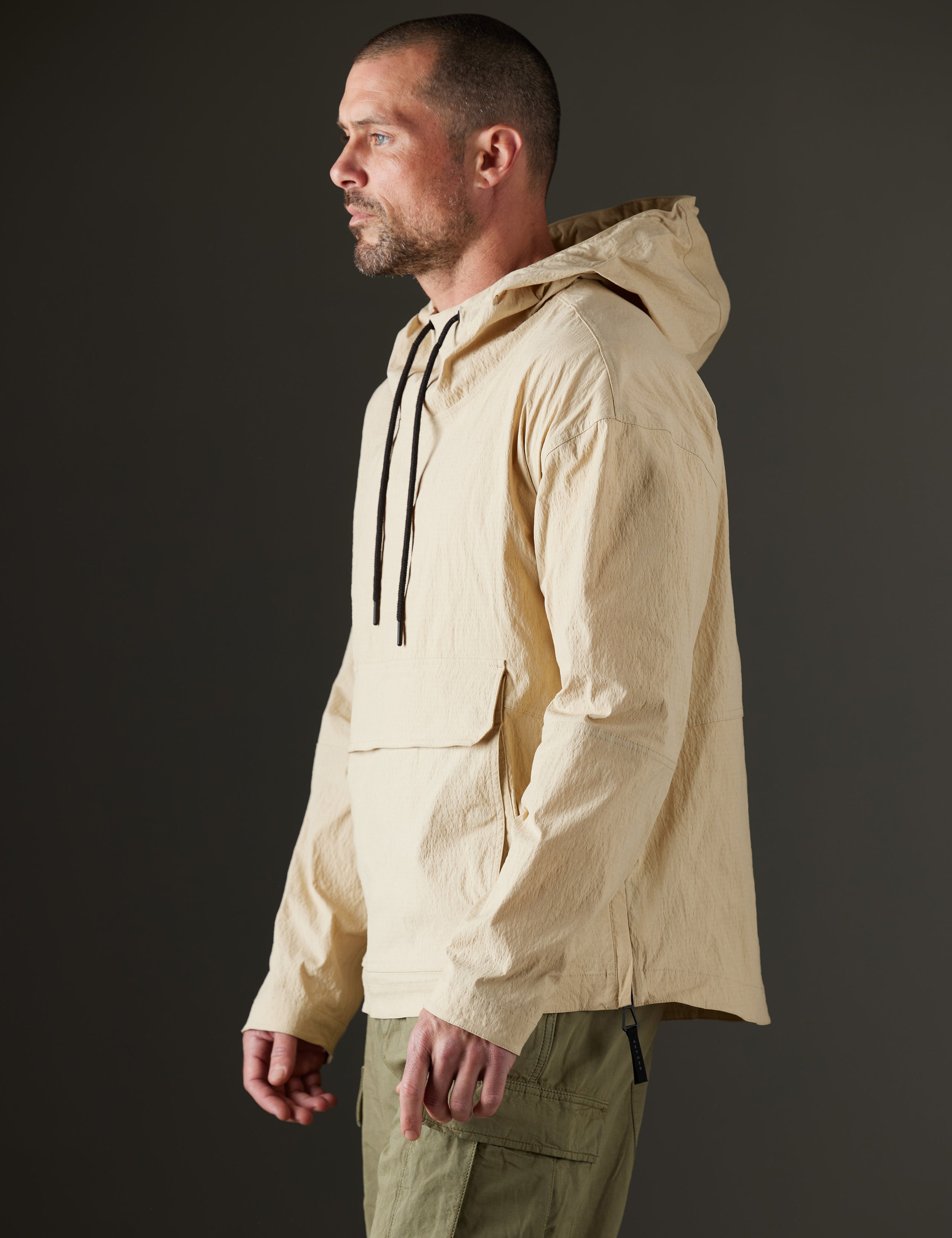 Side profile body view of man wearing Harrier Anorak in Desert Tan from AETHER Apparel.