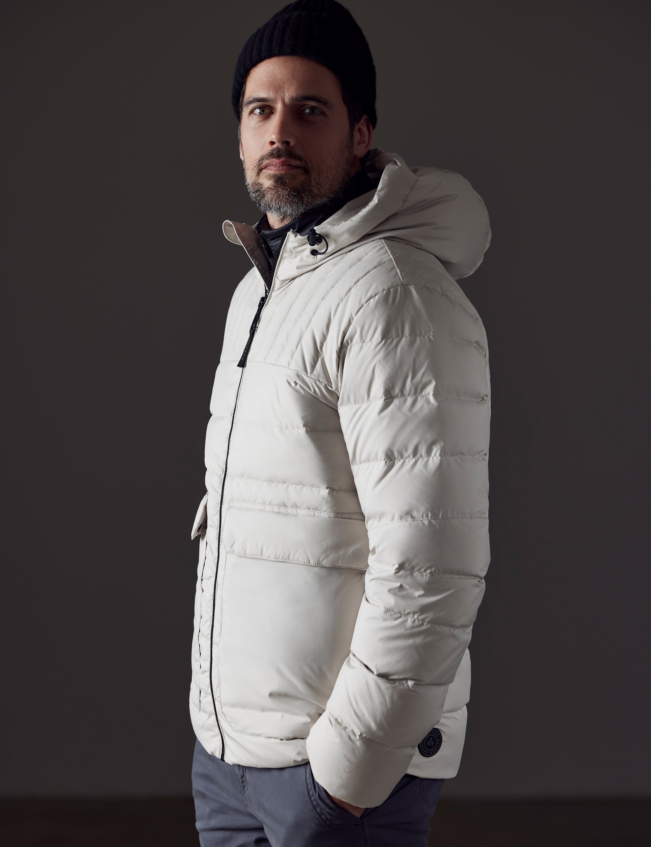 Side profile body view of man wearing Hudson Down Jacket in Bone White from AETHER Apparel.