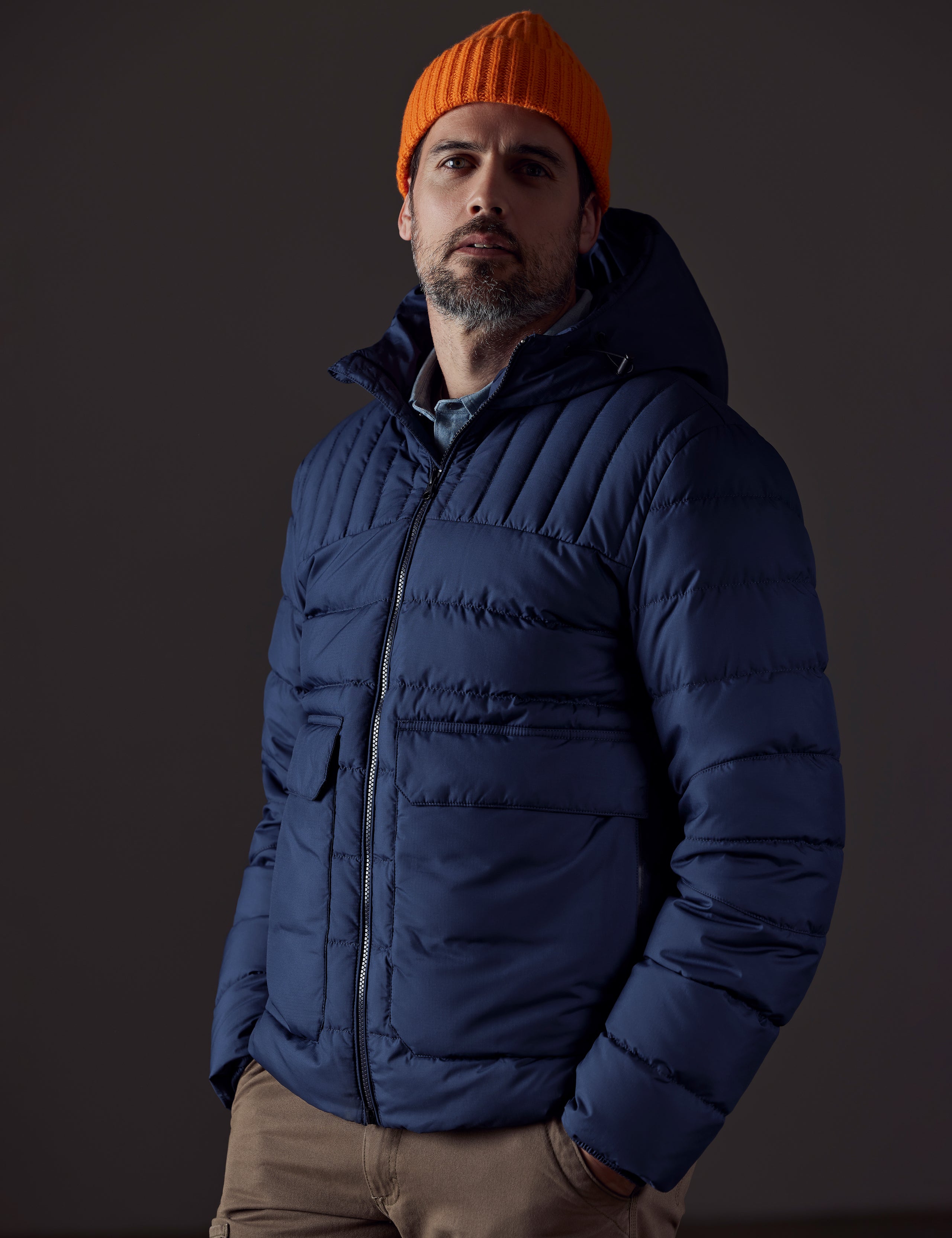 Front 3/4 body view of man with hands in pant pockets wearing Hudson Down Jacket in Total Eclipse dark blue from AETHER Apparel.