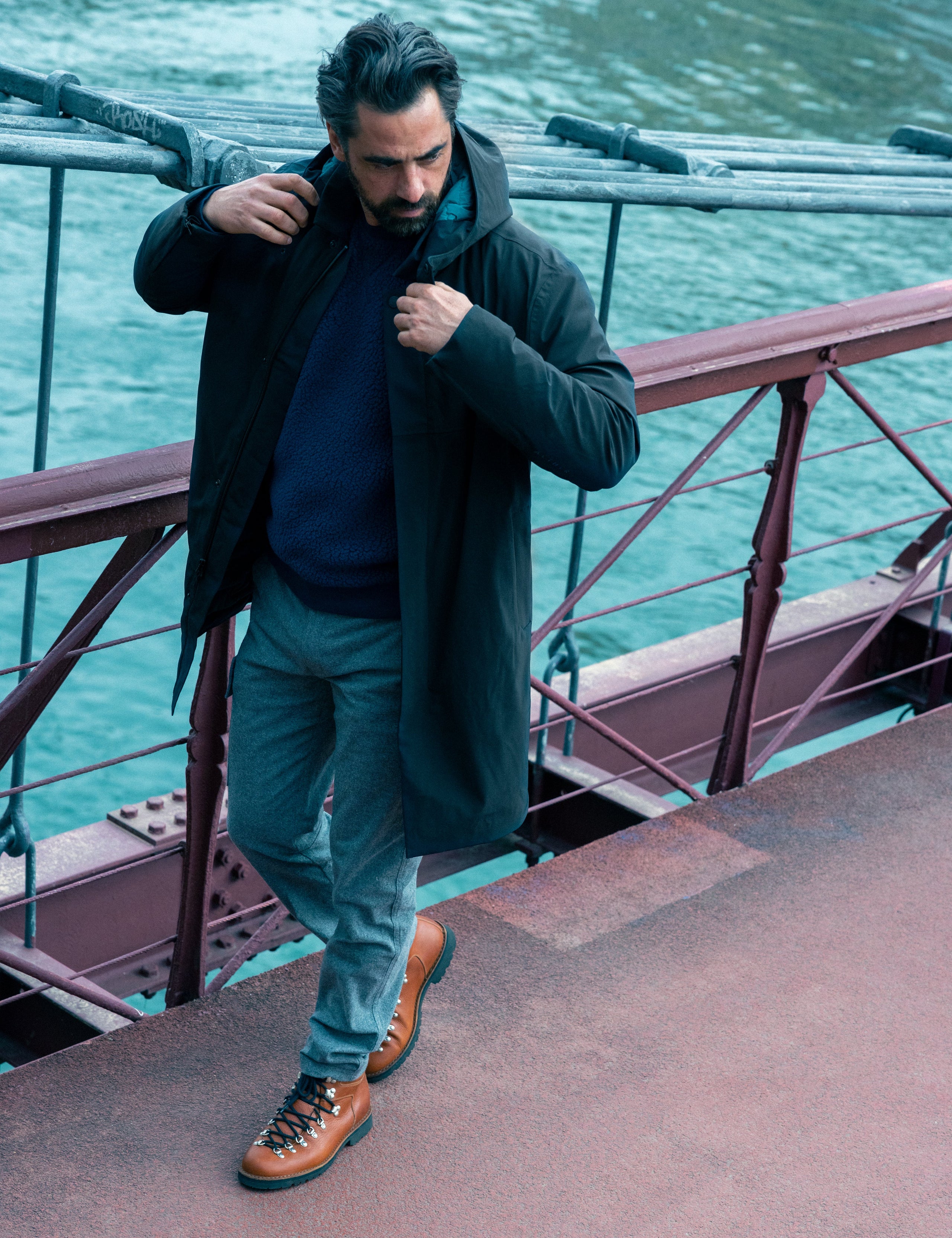 Outdoor lifestyle image of man walking on bridge wearing Isaac Jacket in Onyx Black from AETHER Apparel.