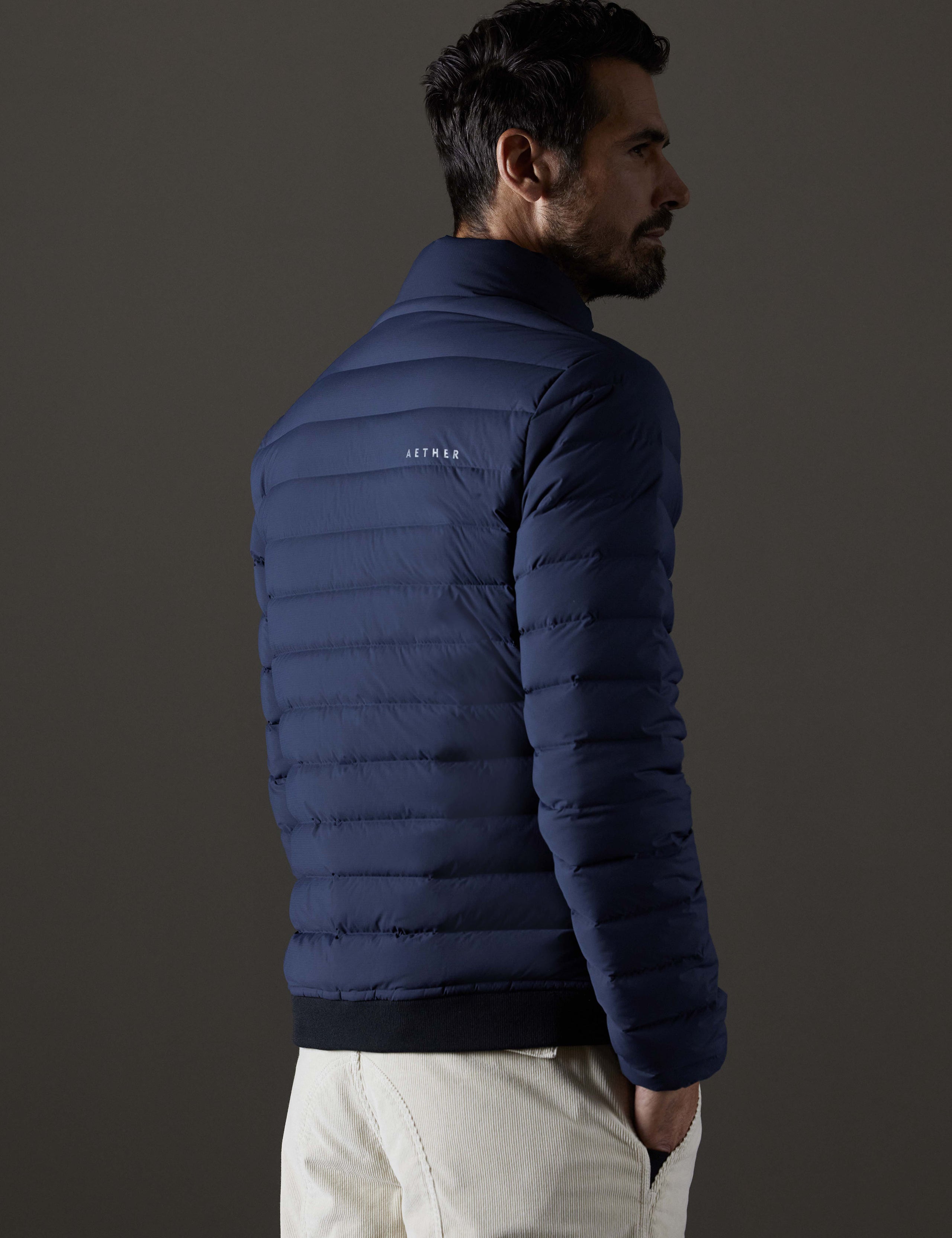 Rear 3/4 body view of man wearing Launch Full-Zip Jacket NH in Total Eclipse dark blue from AETHER Apparel.