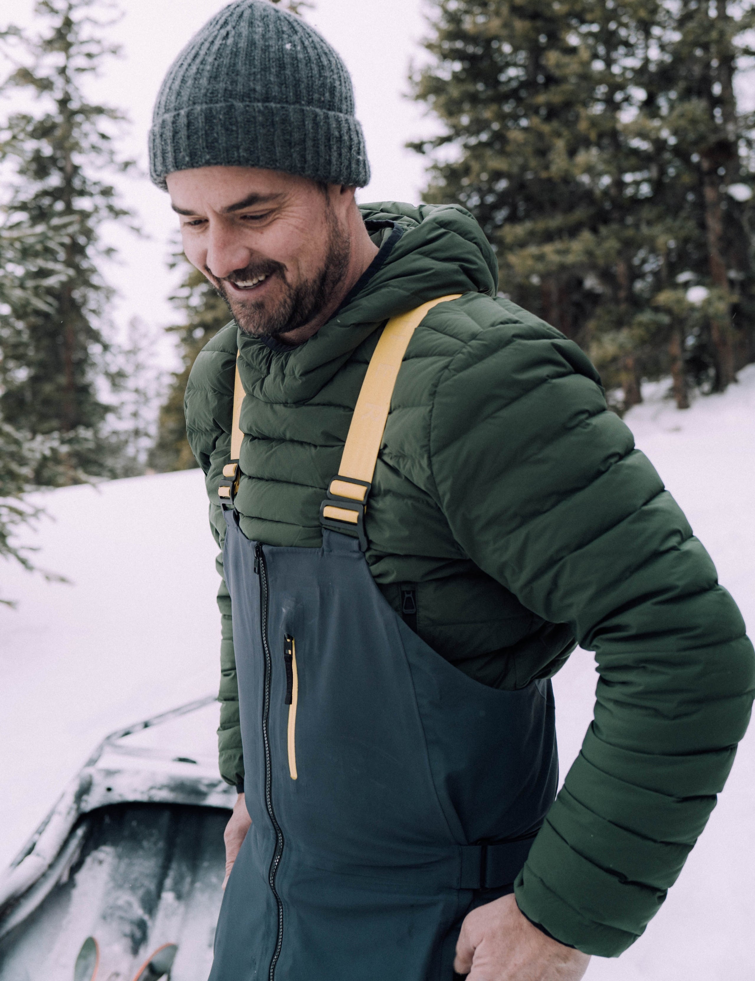 Outdoor lifestyle image of man on snowy hillside wearing Launch Pullover in Duffle Green from AETHER Apparel.