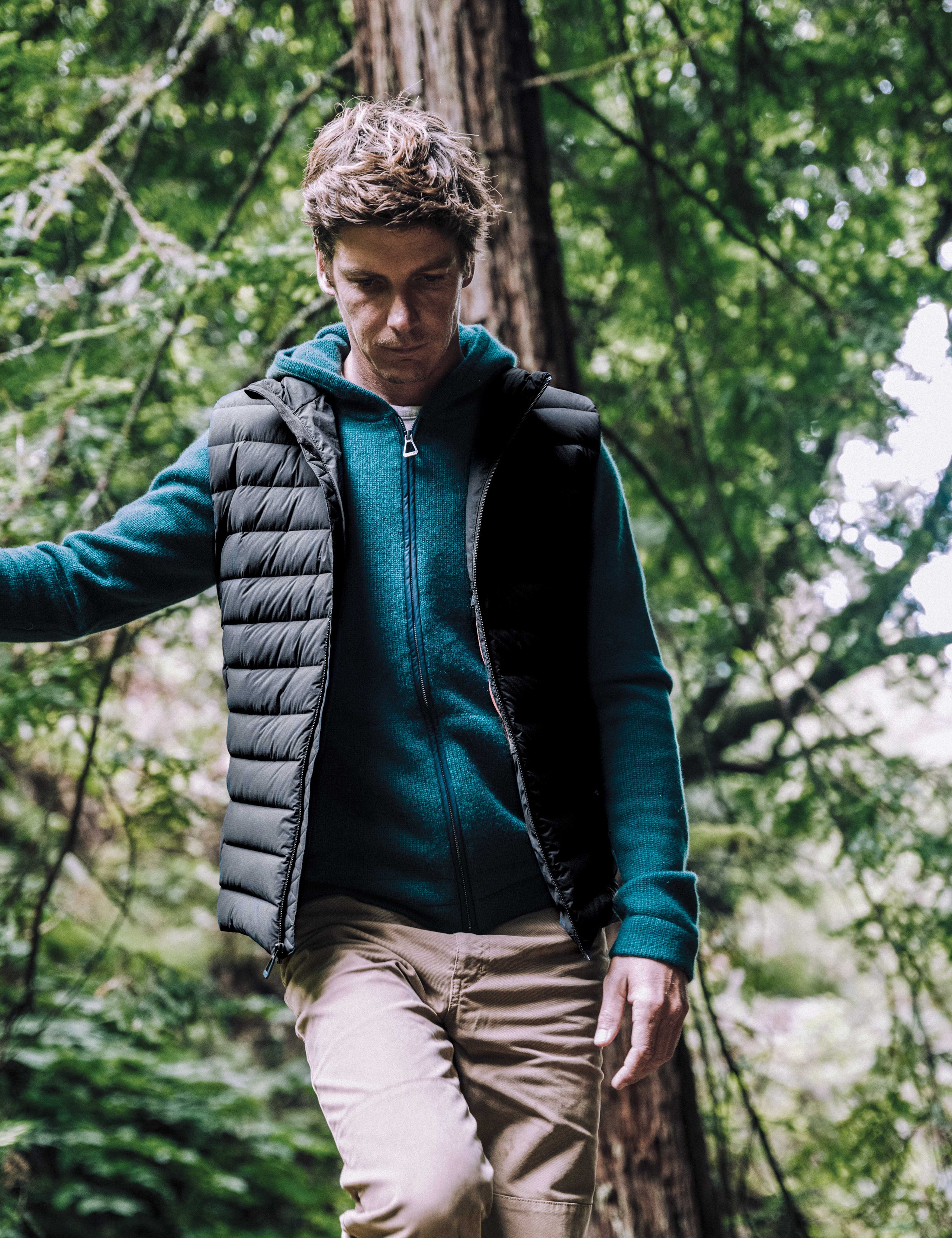 Outdoor lifestyle image of man walking through woods wearing Launch Vest in Onyx Black from AETHER Apparel.