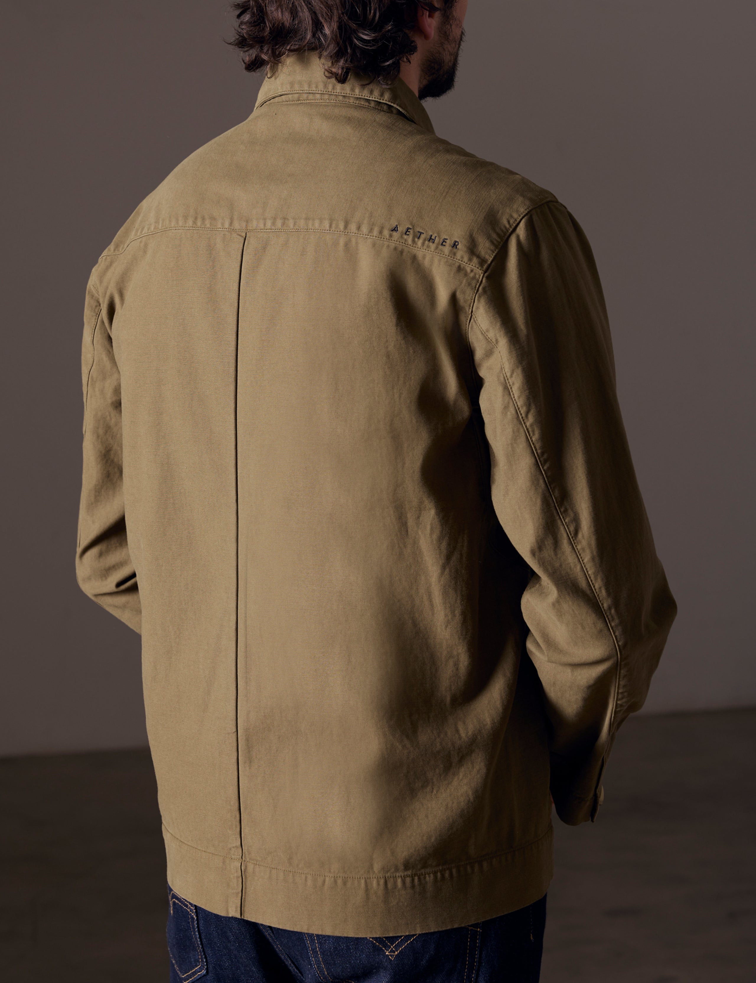 Rear 3/4 body view of man wearing Mesa Jacket in Command Green from AETHER Apparel.