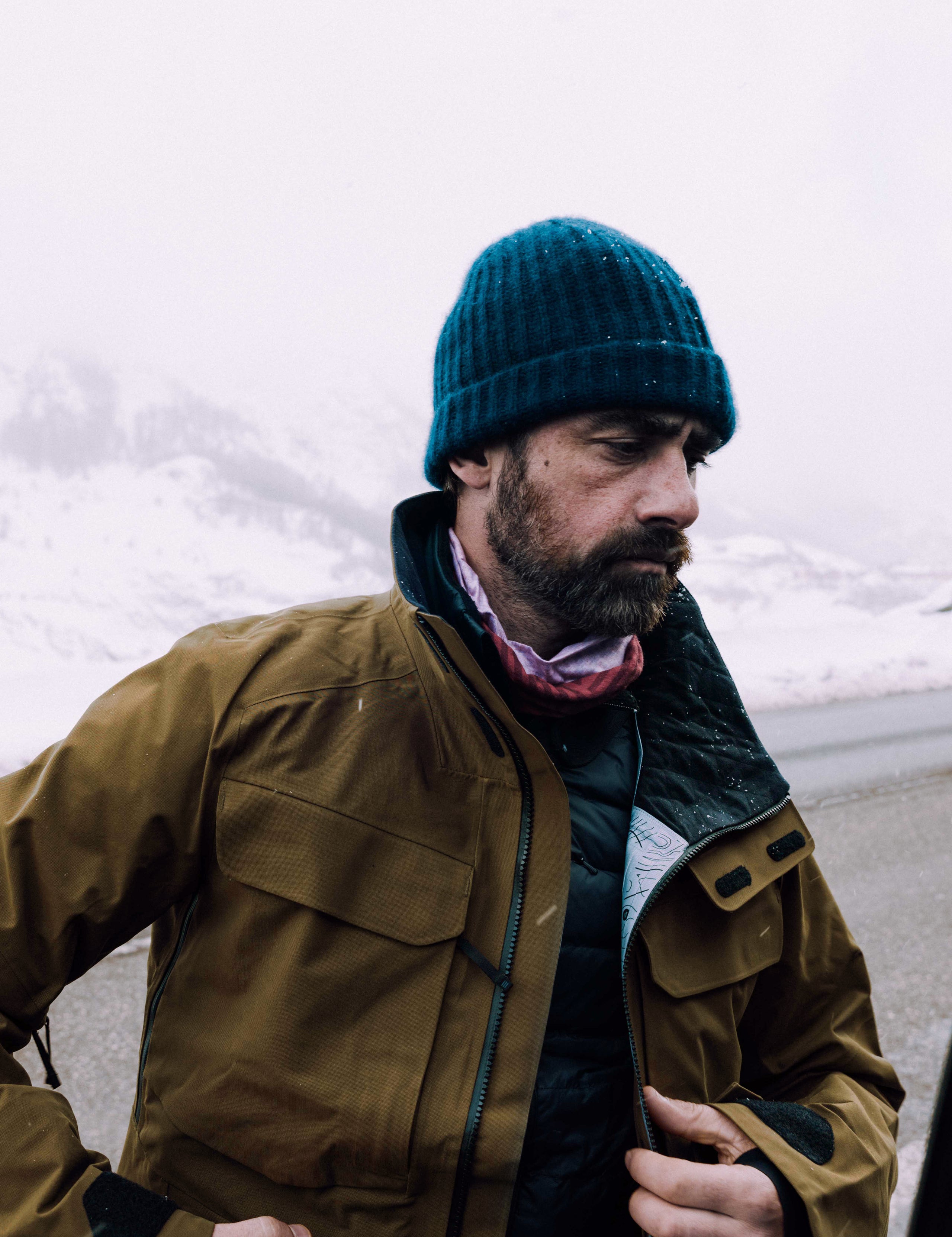 Outdoor lifestyle image of man standing on mountain wearing Mission Snow Shell in Command Green from AETHER Apparel.