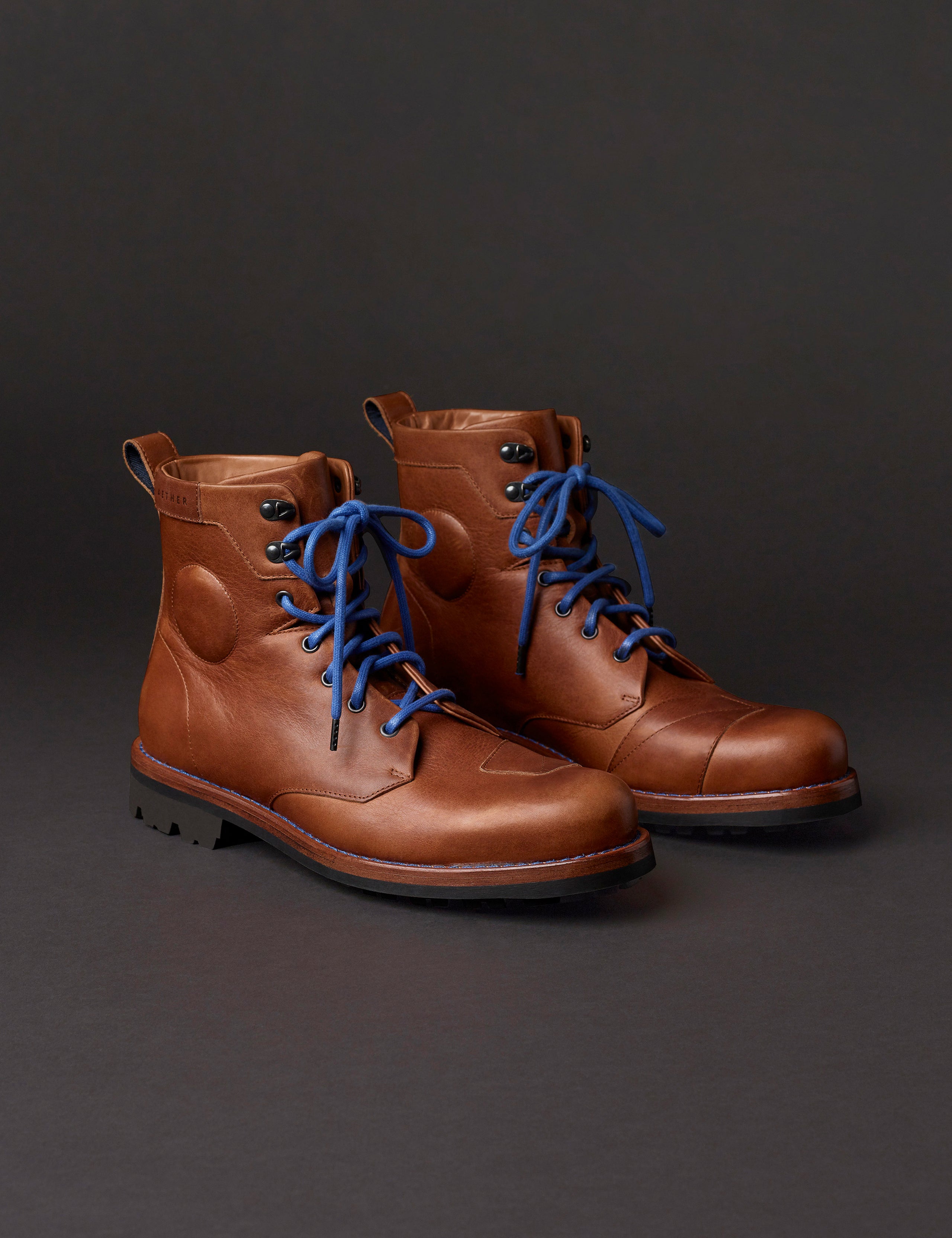 Front angled view of man wearing AETHER Moto Boot in Tan with blue laces from AETHER Apparel.