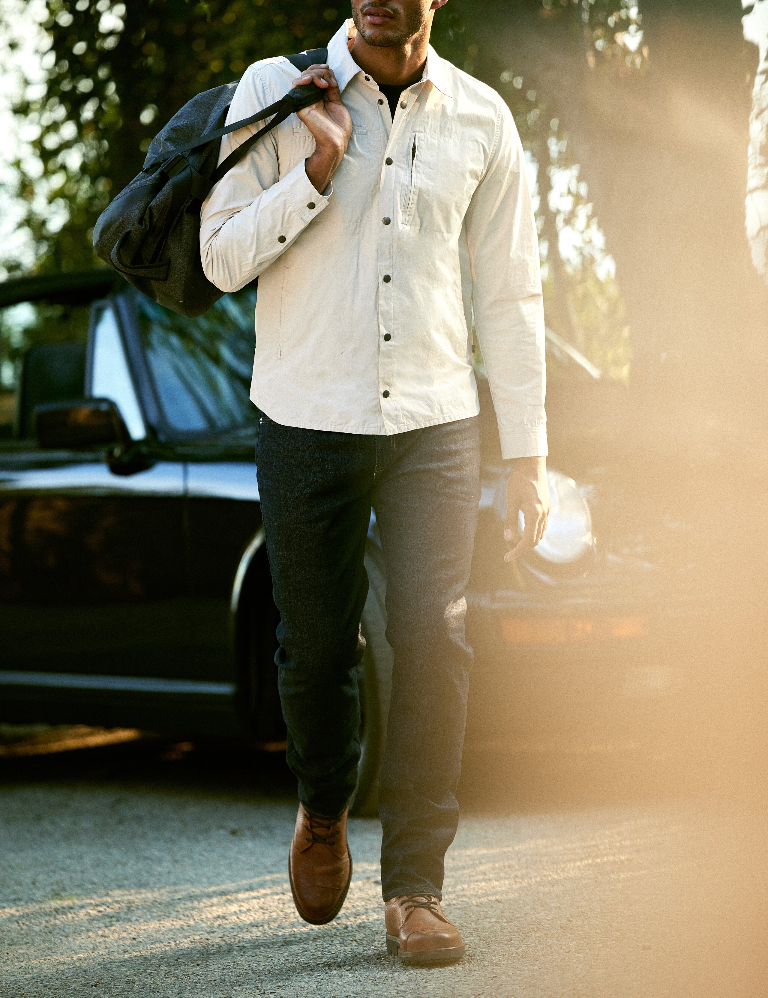 Outdoor lifestyle image of man walking with duffle bag over shoulder wearing AETHER Moto Boot in Tan from AETHER Apparel.