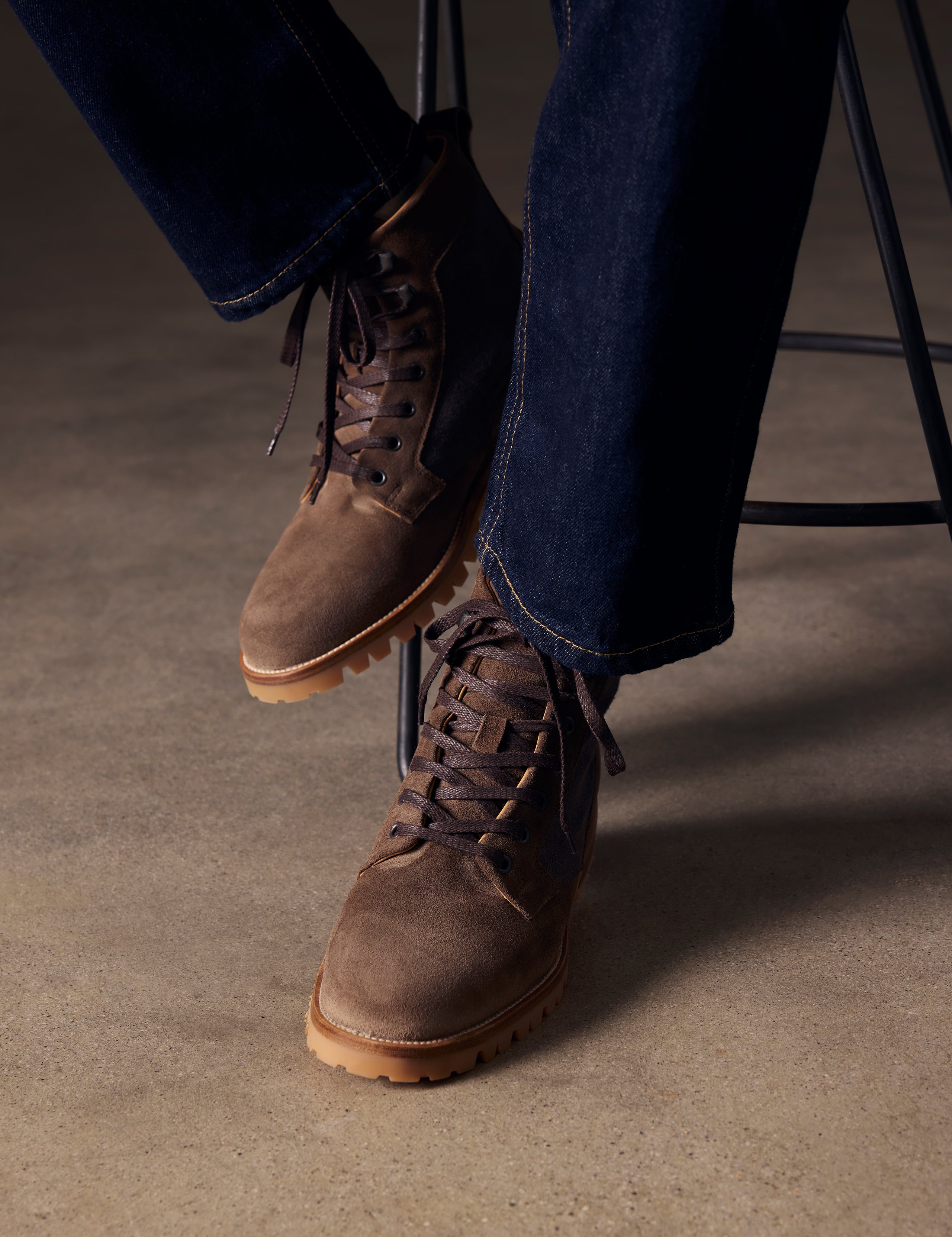Closeup lifestyle image of feet of man sitting on stool wearing Ojai City Boot in Bison Brown suede and canvas from AETHER Apparel.