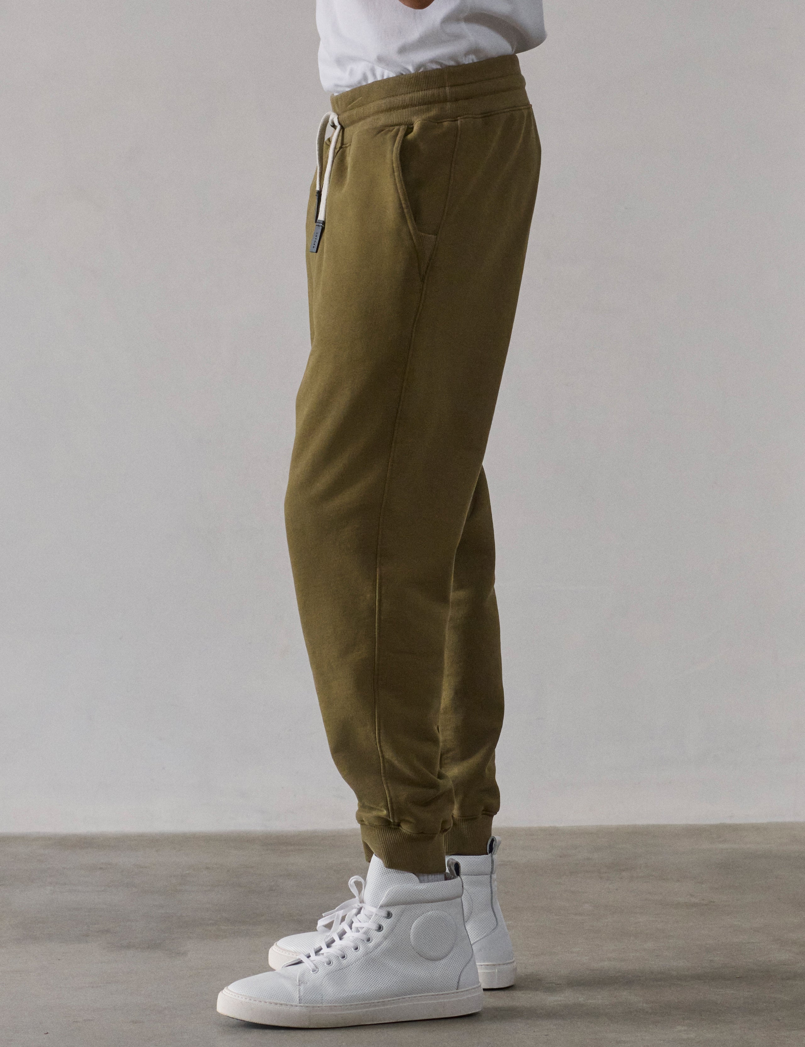 Left side profile lower-body view of man wearing Osa Cuffed Sweatpant in Command Green from AETHER Apparel.