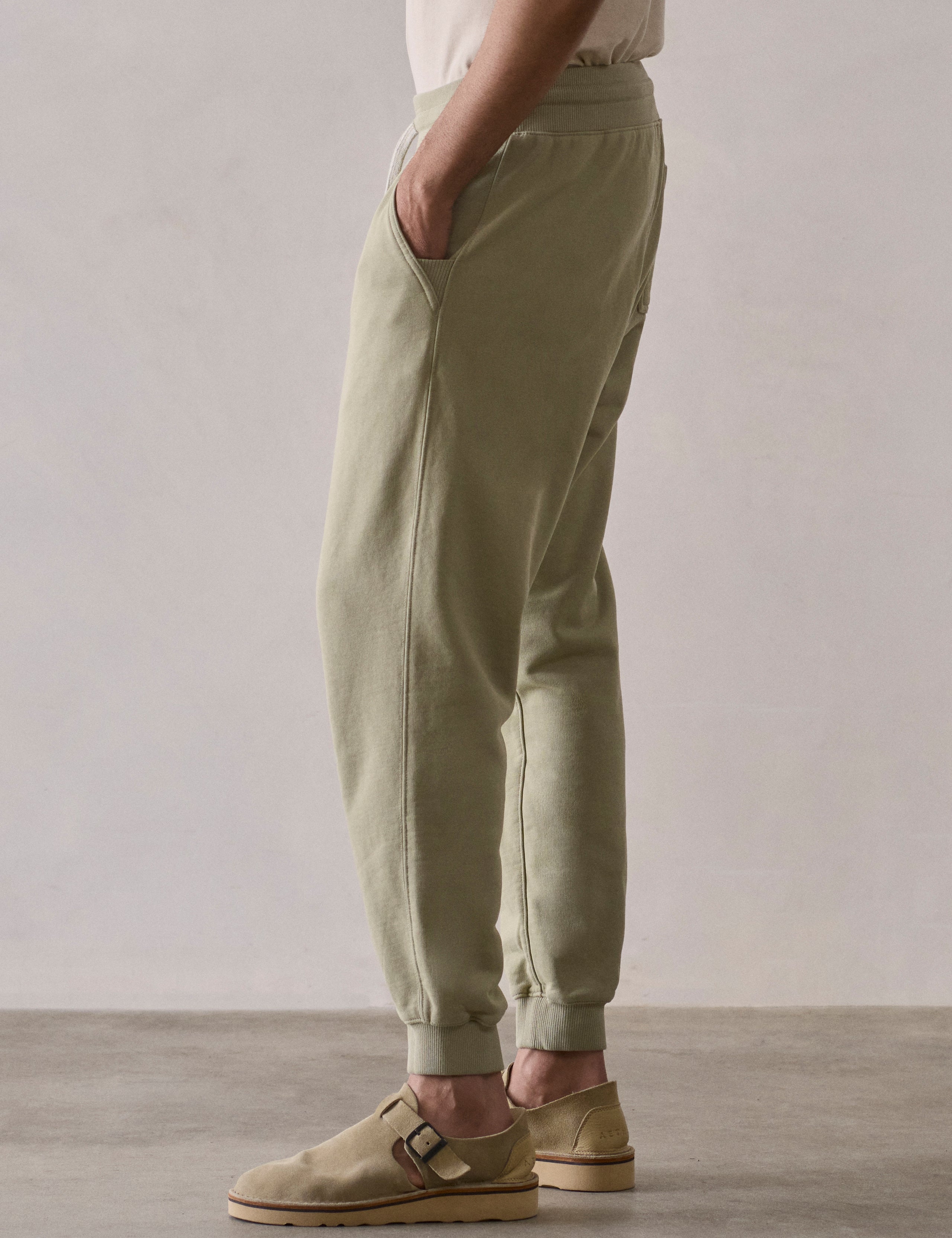 Left side lower body profile view of man wearing Osa Cuffed Sweatpant in Sage Green from AETHER Apparel.