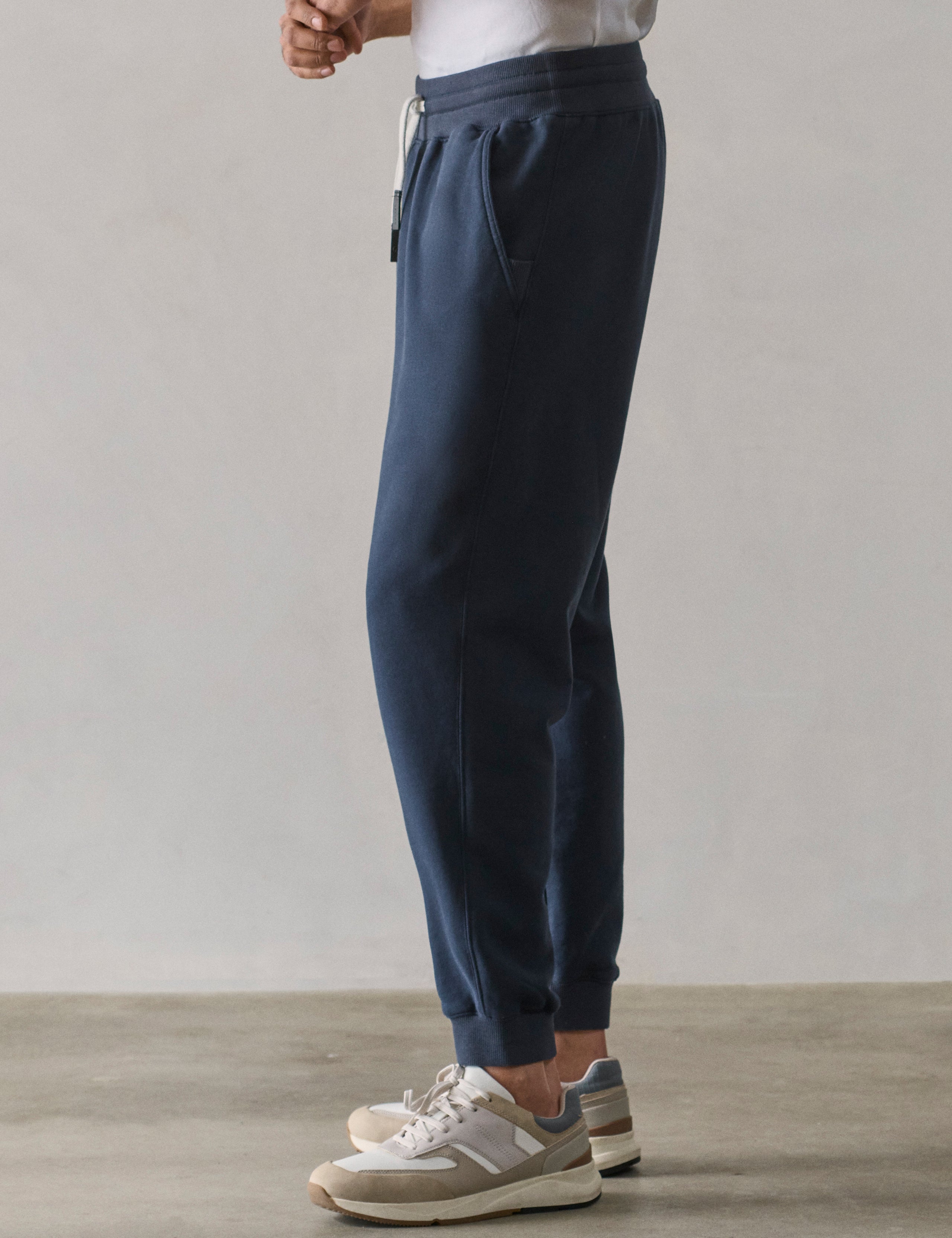 Left side lower body profile view of man wearing Osa Cuffed Sweatpant in Total Eclipse dark blue from AETHER Apparel.