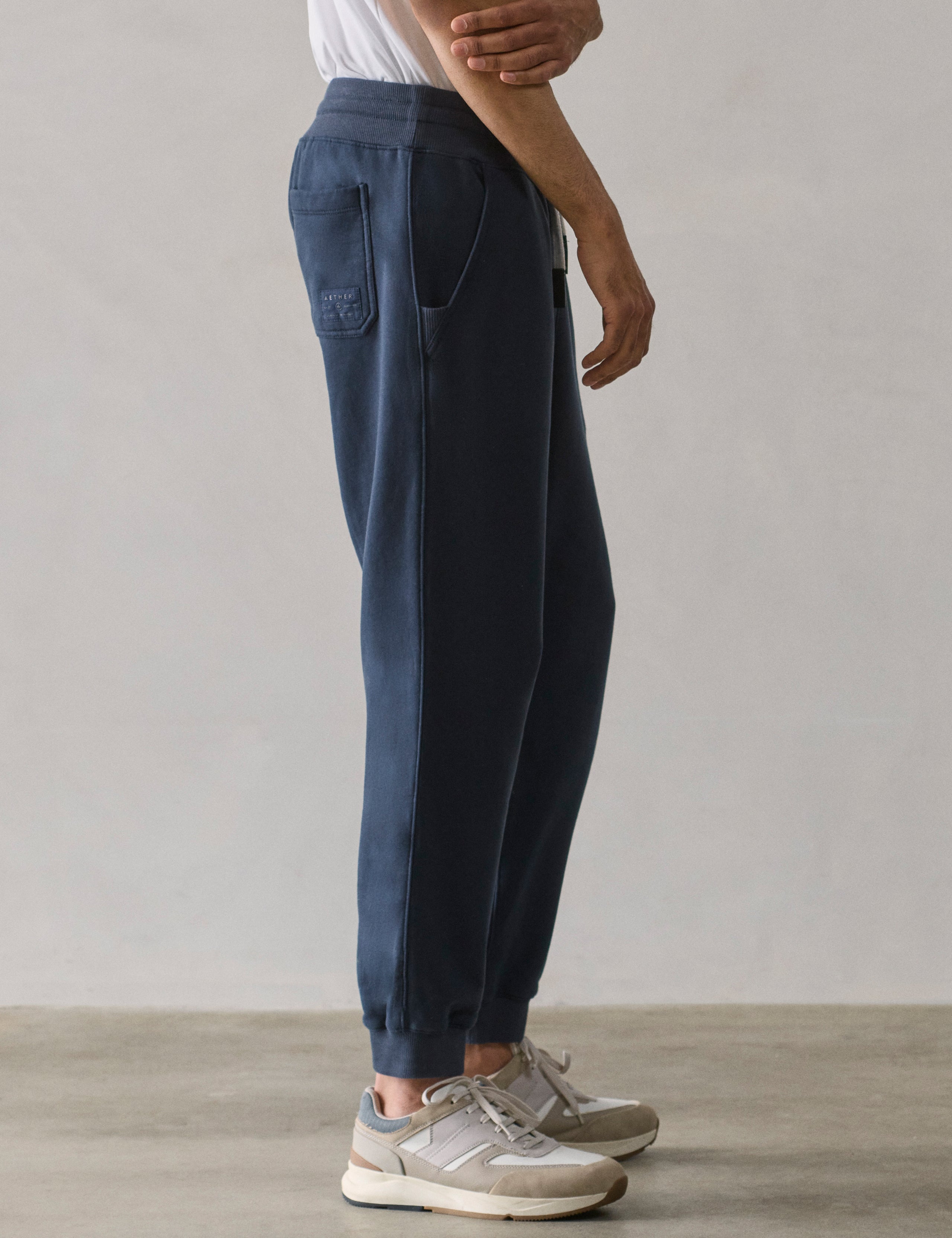 Right side lower body profile view of man wearing Osa Cuffed Sweatpant in Total Eclipse dark blue from AETHER Apparel.
