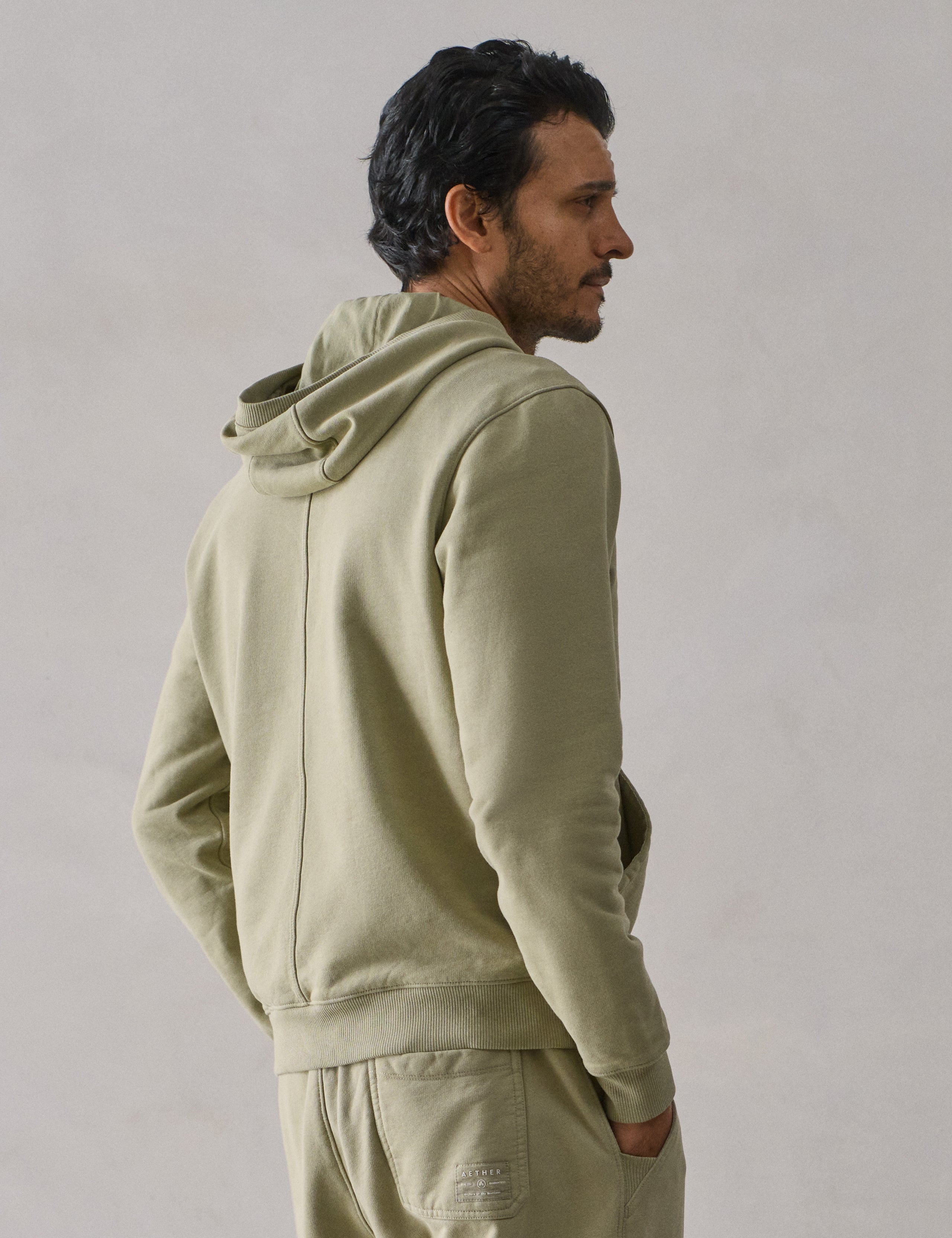 Rear 3/4 upper body view of man wearing Osa Pullover Hoodie in Sage Green from AETHER Apparel.