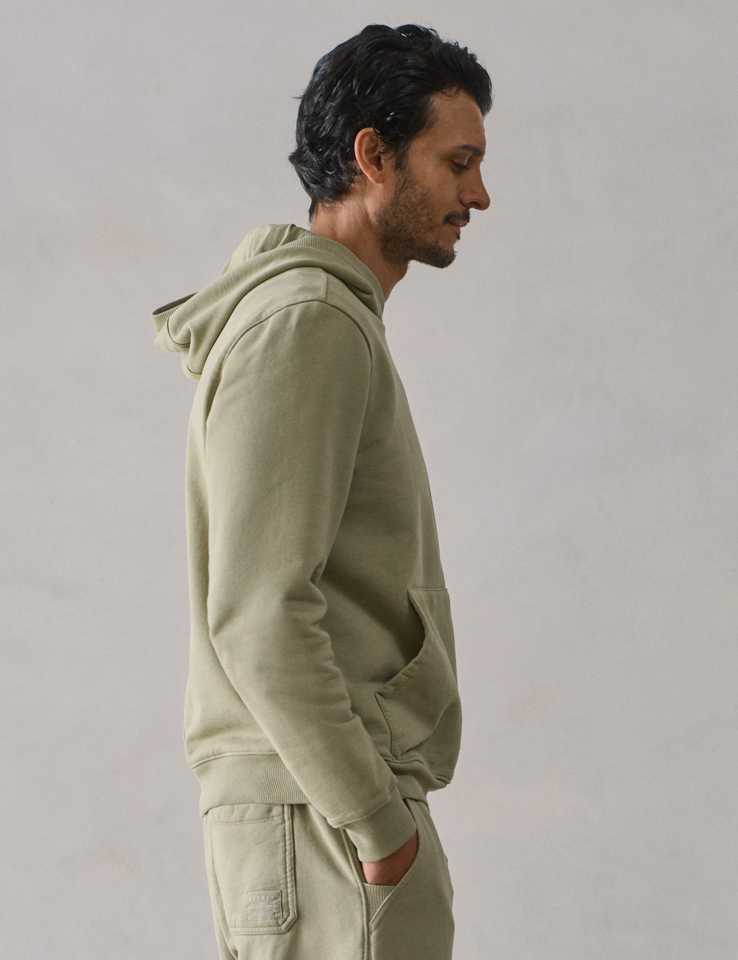 Right side upper body profile view of man wearing Osa Pullover Hoodie in Sage Green from AETHER Apparel.