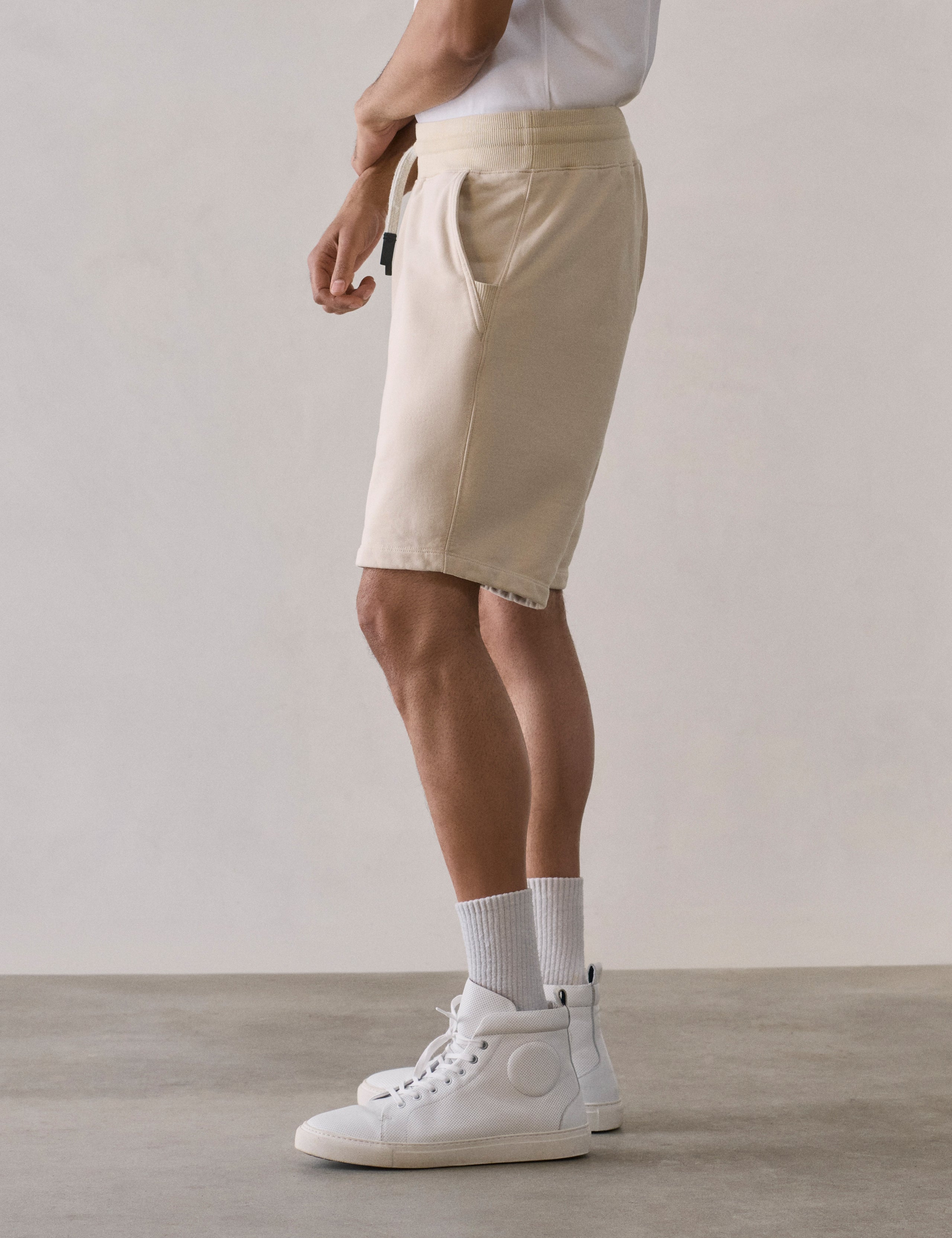 Left side lower body profile view of man wearing Osa Sweatshort in Bone white from AETHER Apparel.